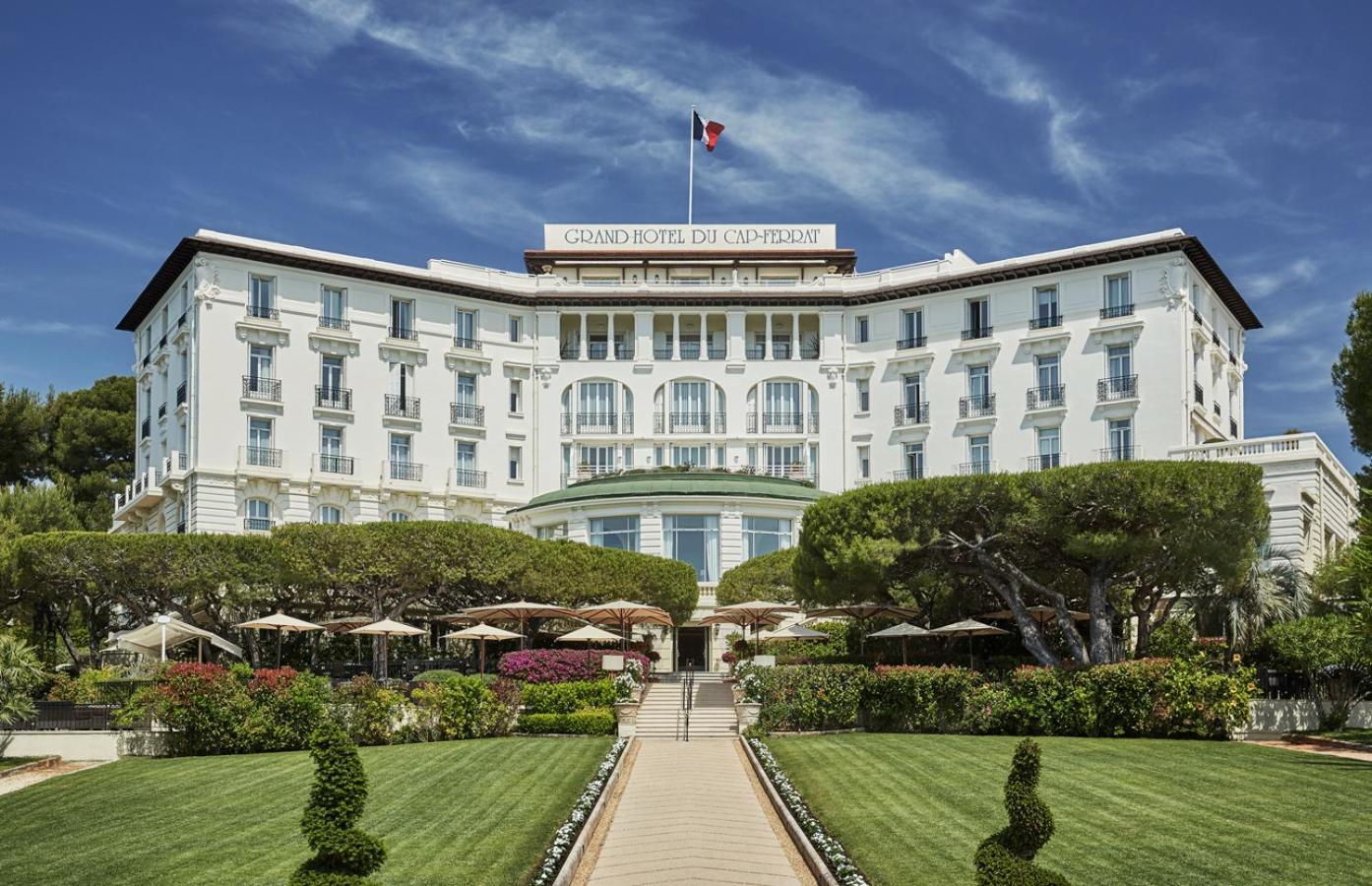 Manicured gardens frame the Belle Époque grandeur of this legendary Riviera palace, where striped umbrellas dot terraces overlooking the Mediterranean's azure expanse.