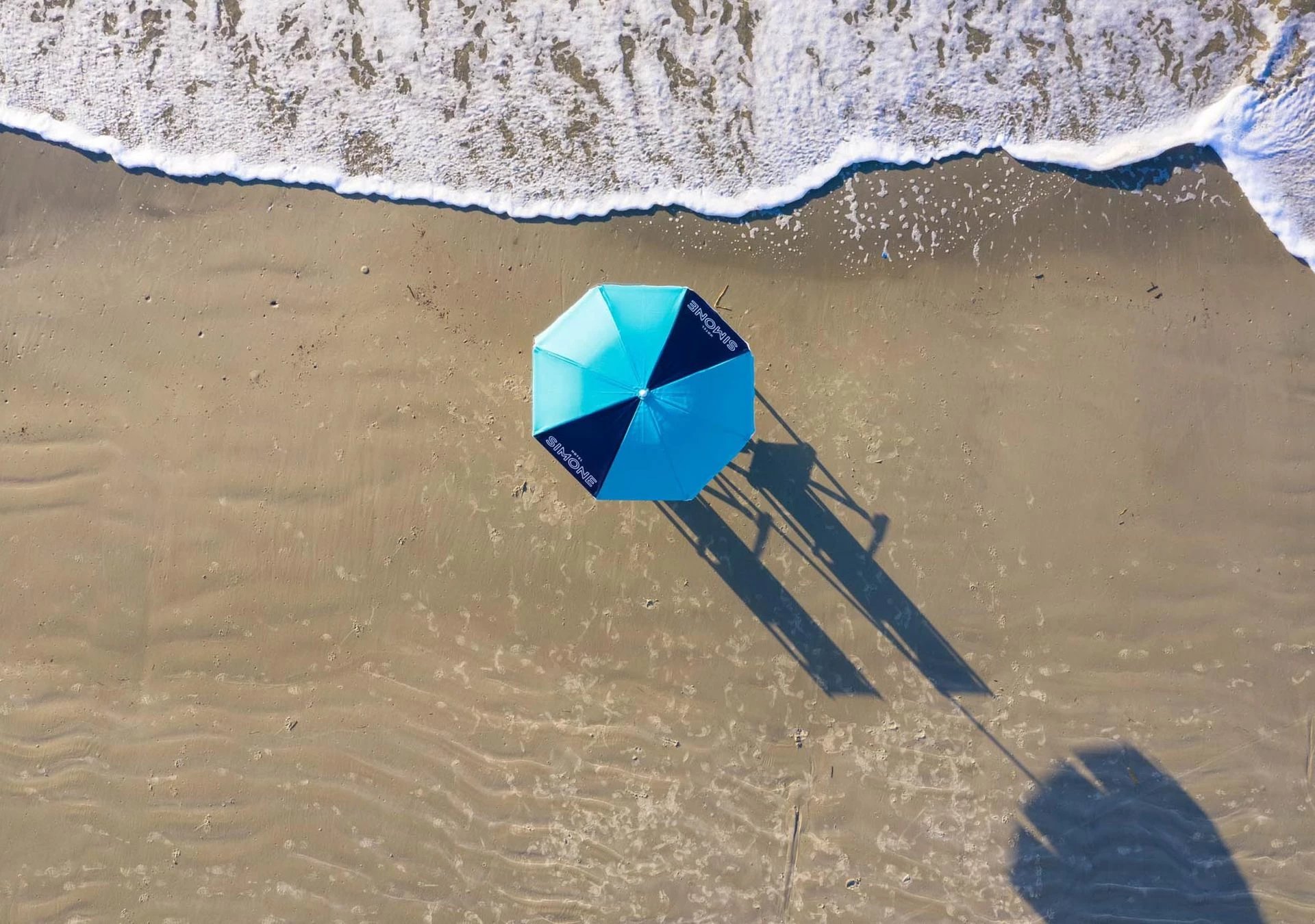 Branded beach umbrellas cast bold shadows across pristine sand as waves gently lap the shoreline, creating an intimate seaside sanctuary for guests.