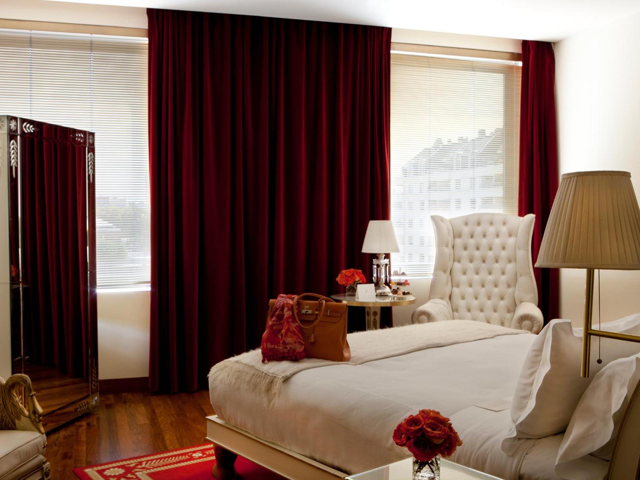 Crimson velvet drapes frame city views while tufted wingback chairs and warm lamplight create an intimate Buenos Aires sanctuary above the bustling streets below.