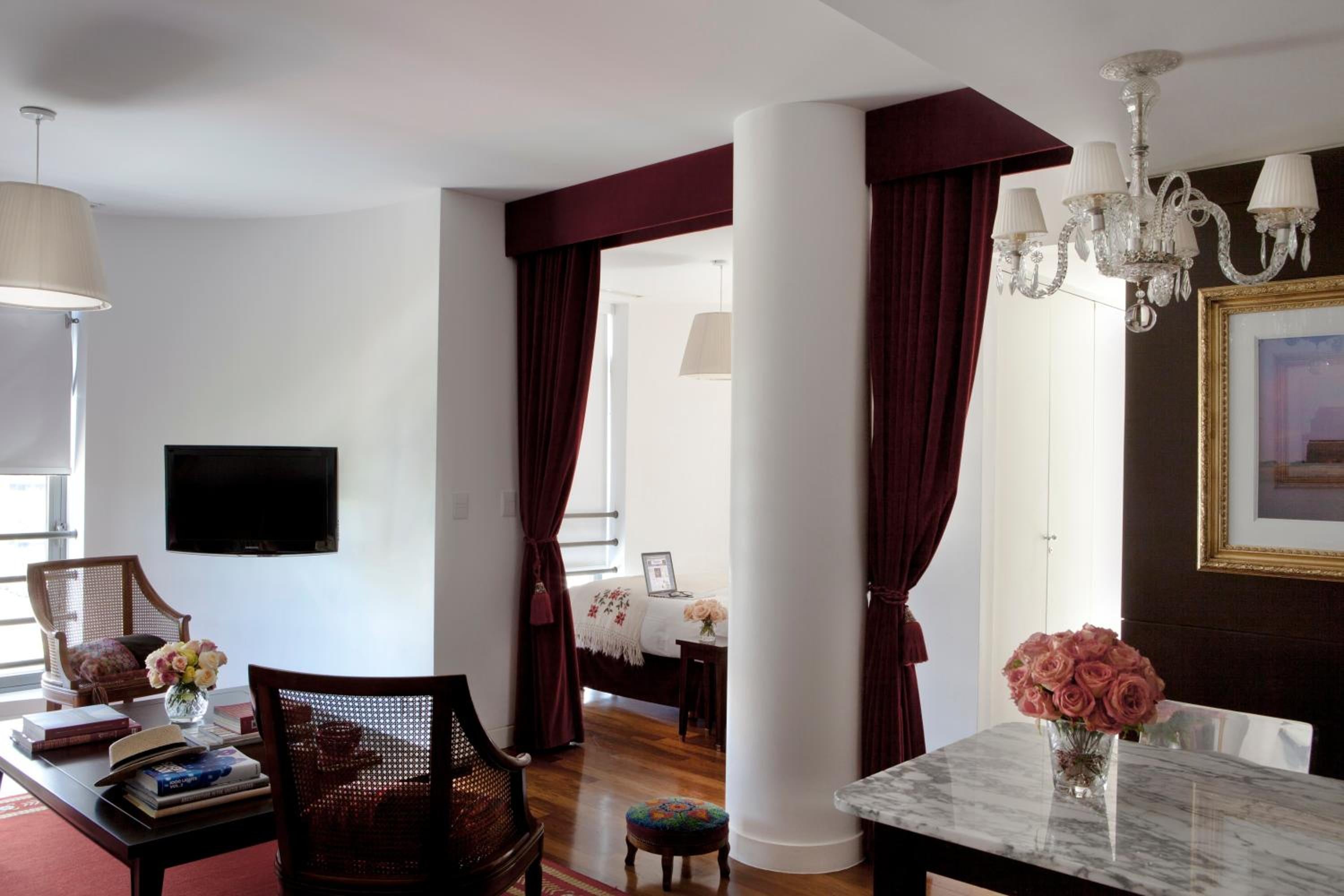 Burgundy velvet drapes frame city views while crystal chandeliers cast warm light over marble surfaces and hand-picked roses in this sophisticated suite.