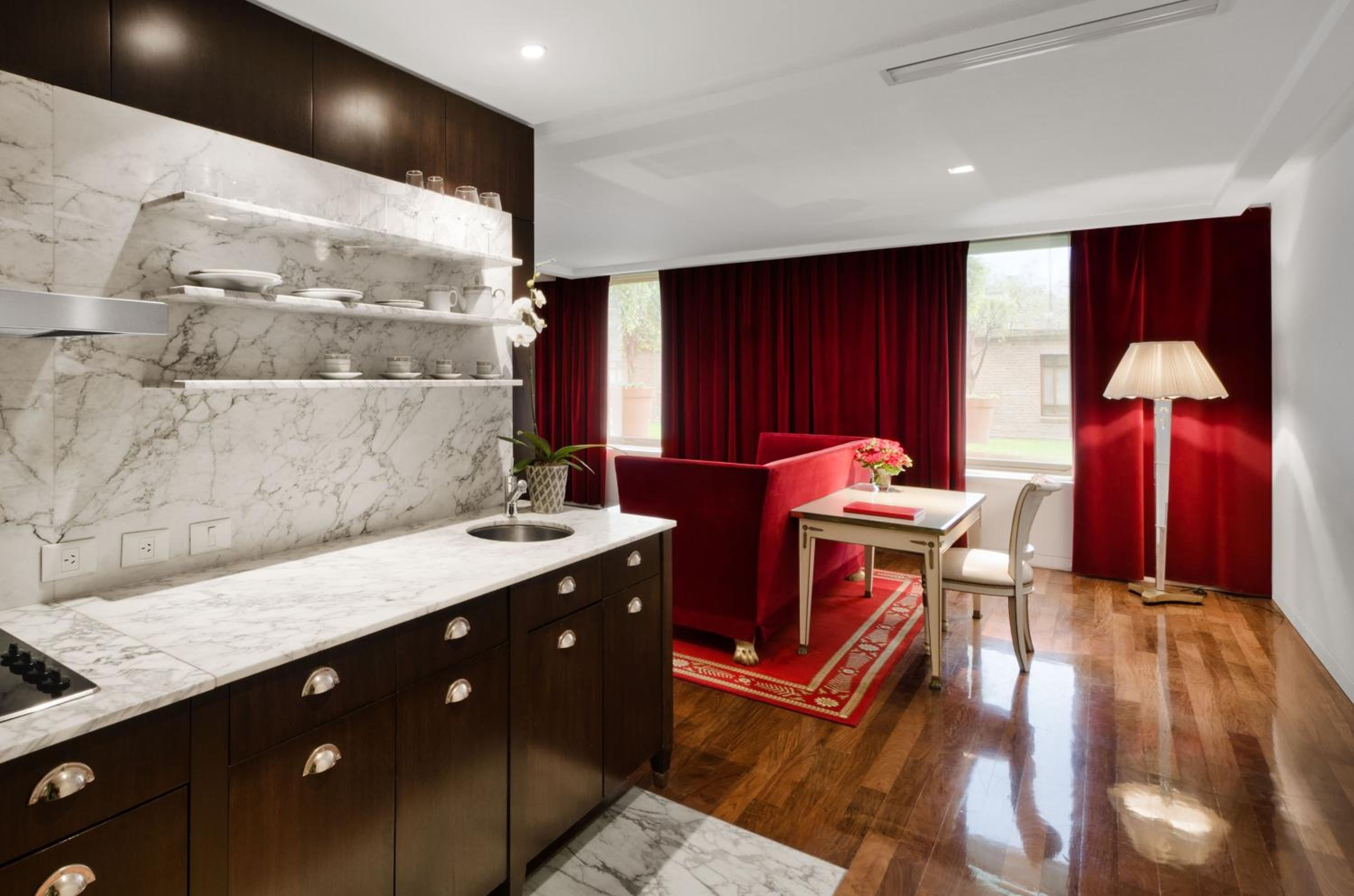 Marble countertops gleam against dark cabinetry while crimson velvet curtains frame this sophisticated suite, where Buenos Aires luxury meets intimate residential charm.