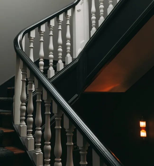 Graceful white balusters curve along the hotel's traditional staircase, where warm amber light pools beneath dark wood treads, creating intimate shadows that whisper of old-world Portuguese elegance.