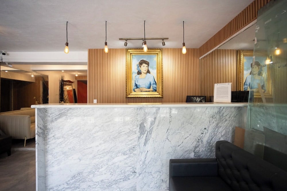 Warm wood slats and veined marble create an inviting reception area, where vintage portraiture and Edison bulb pendants blend contemporary comfort with thoughtful character.