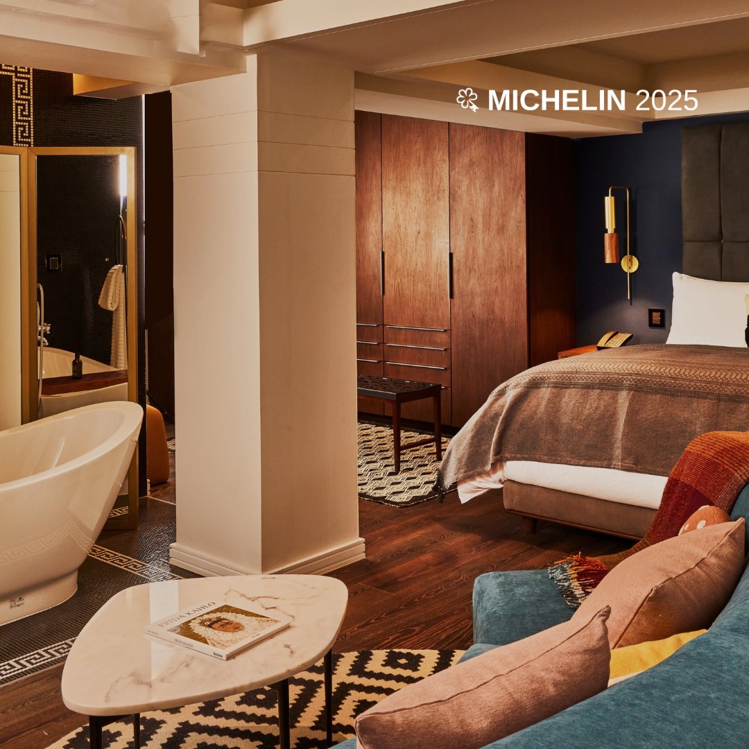 Warm walnut cabinetry and geometric textiles create an inviting sanctuary where the marble soaking tub becomes a sculptural centerpiece beneath exposed concrete beams.