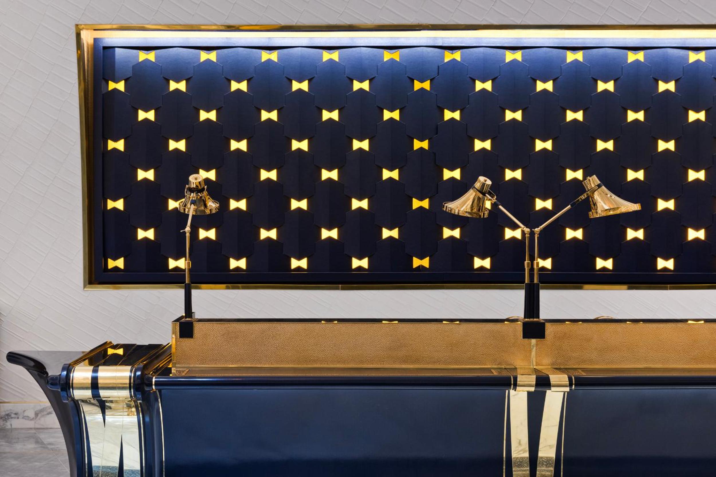 Golden bow-tie studs create a striking geometric pattern against navy blue panels, while polished brass lamps cast warm light over luxurious seating areas.
