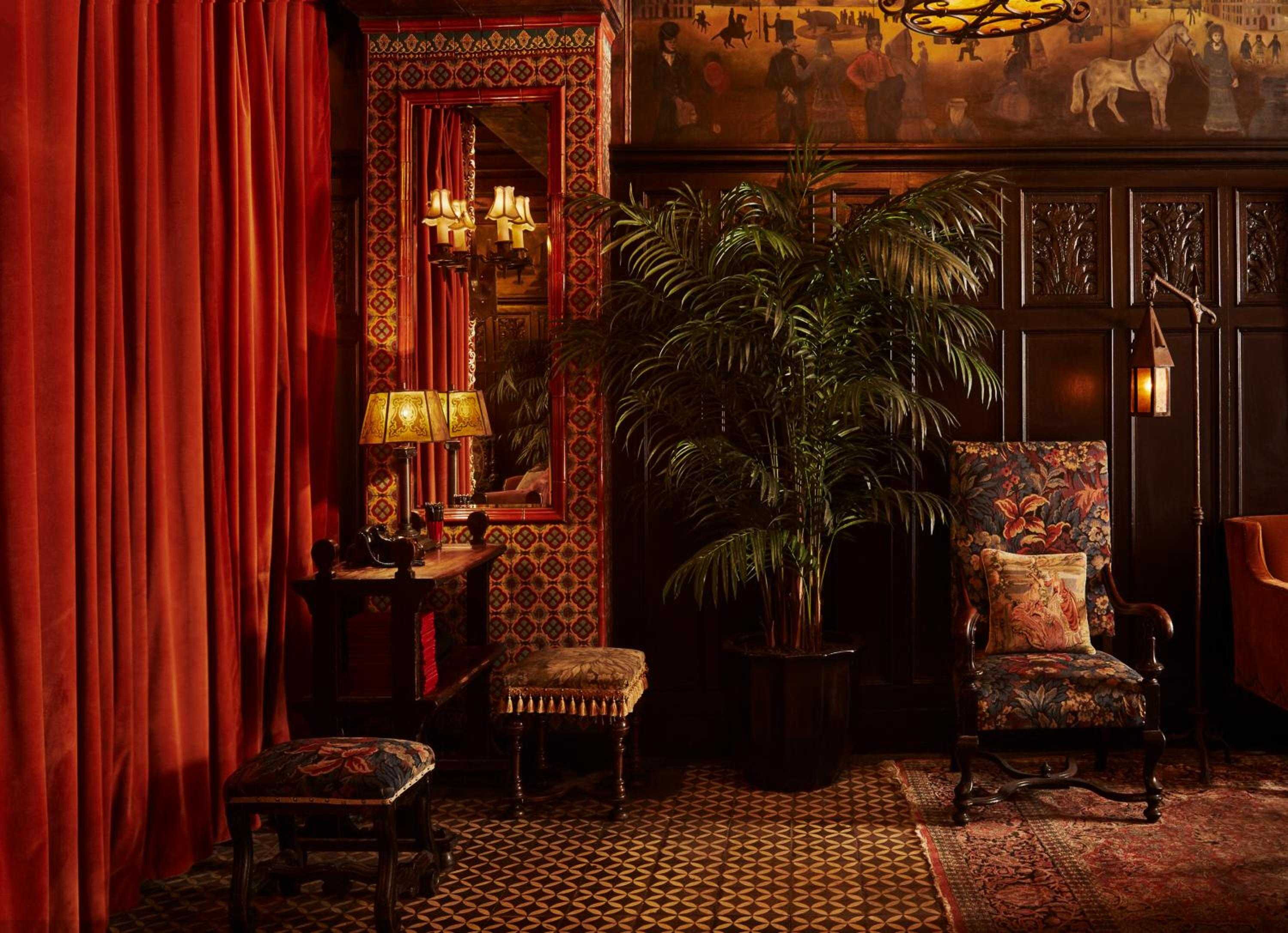 Rich crimson velvet curtains frame an intimate corner where ornate Persian rugs, antique furnishings, and flickering lanterns create an atmospheric Victorian sanctuary.