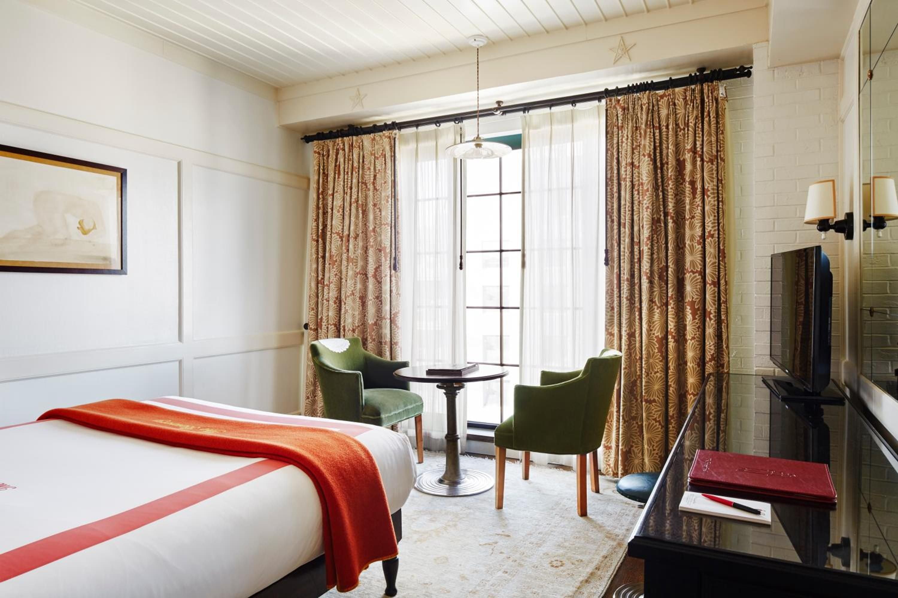 Patterned curtains frame French doors while emerald velvet chairs create an intimate sitting area, blending old-world charm with modern comfort.