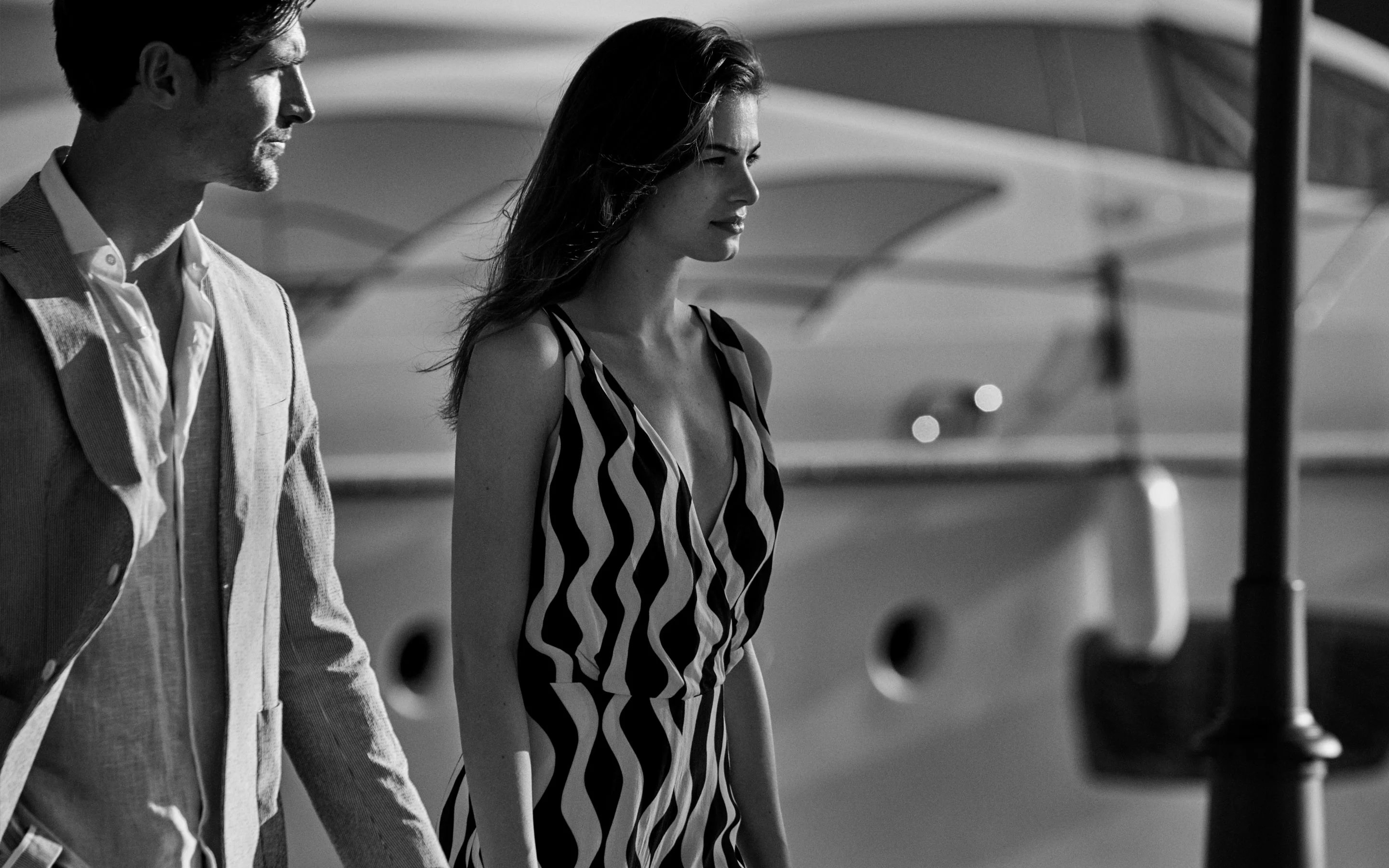 Elegant couples stroll beneath soaring white arches, their sophisticated silhouettes framed against Montenegro's luminous maritime architecture where modern luxury meets Adriatic grandeur.