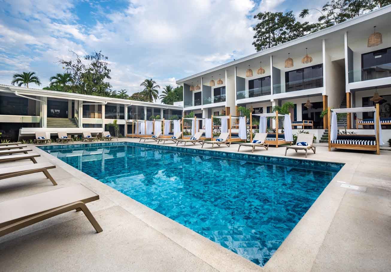 Wicker pendant lights cast gentle shadows over the crystalline pool, where cabanas with navy-striped cushions invite languid afternoons beneath swaying palms.