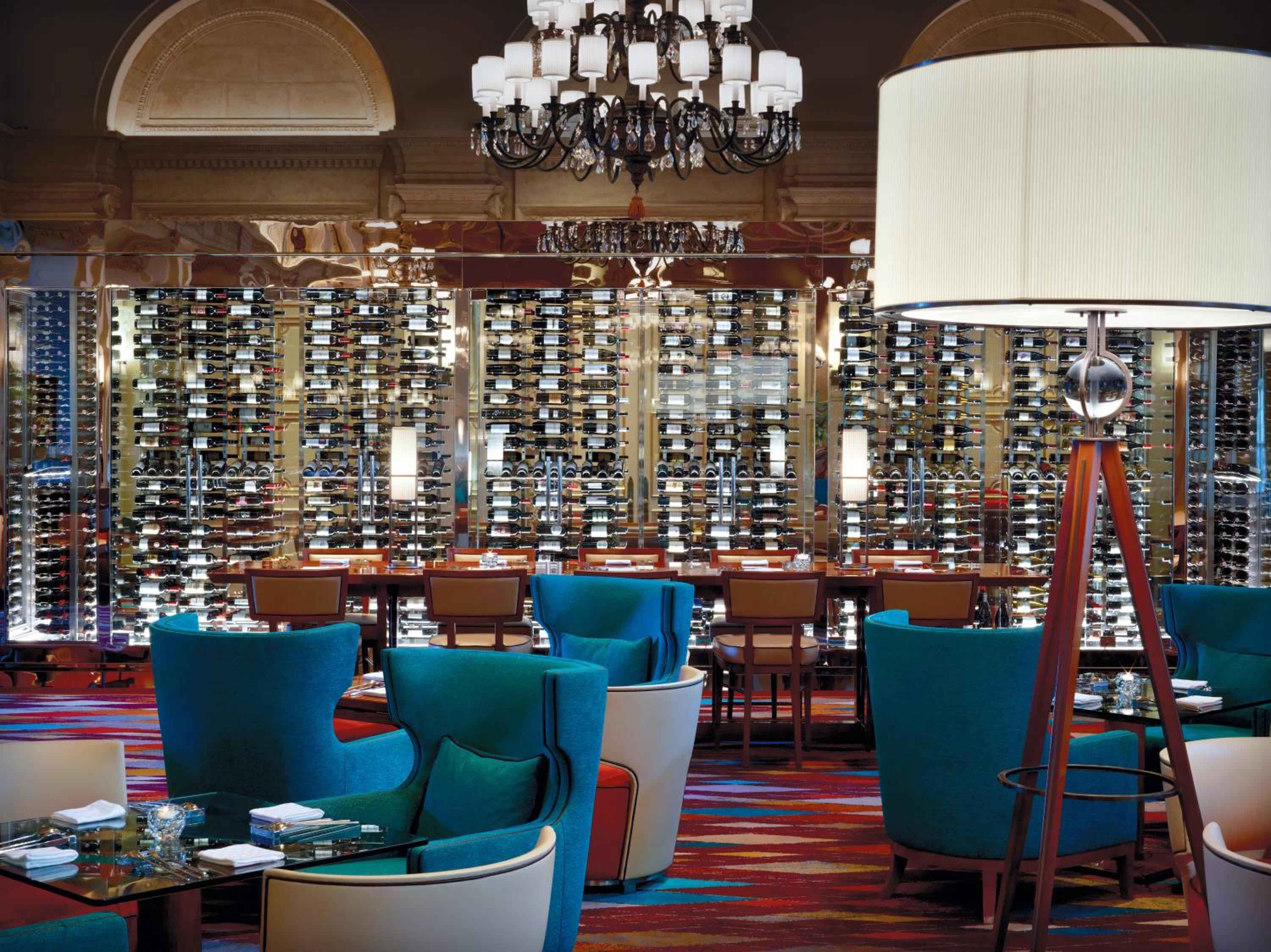 Floor-to-ceiling wine displays create dramatic backdrop for intimate dining, where turquoise velvet chairs and crystal chandeliers blend modern sophistication with classic elegance.