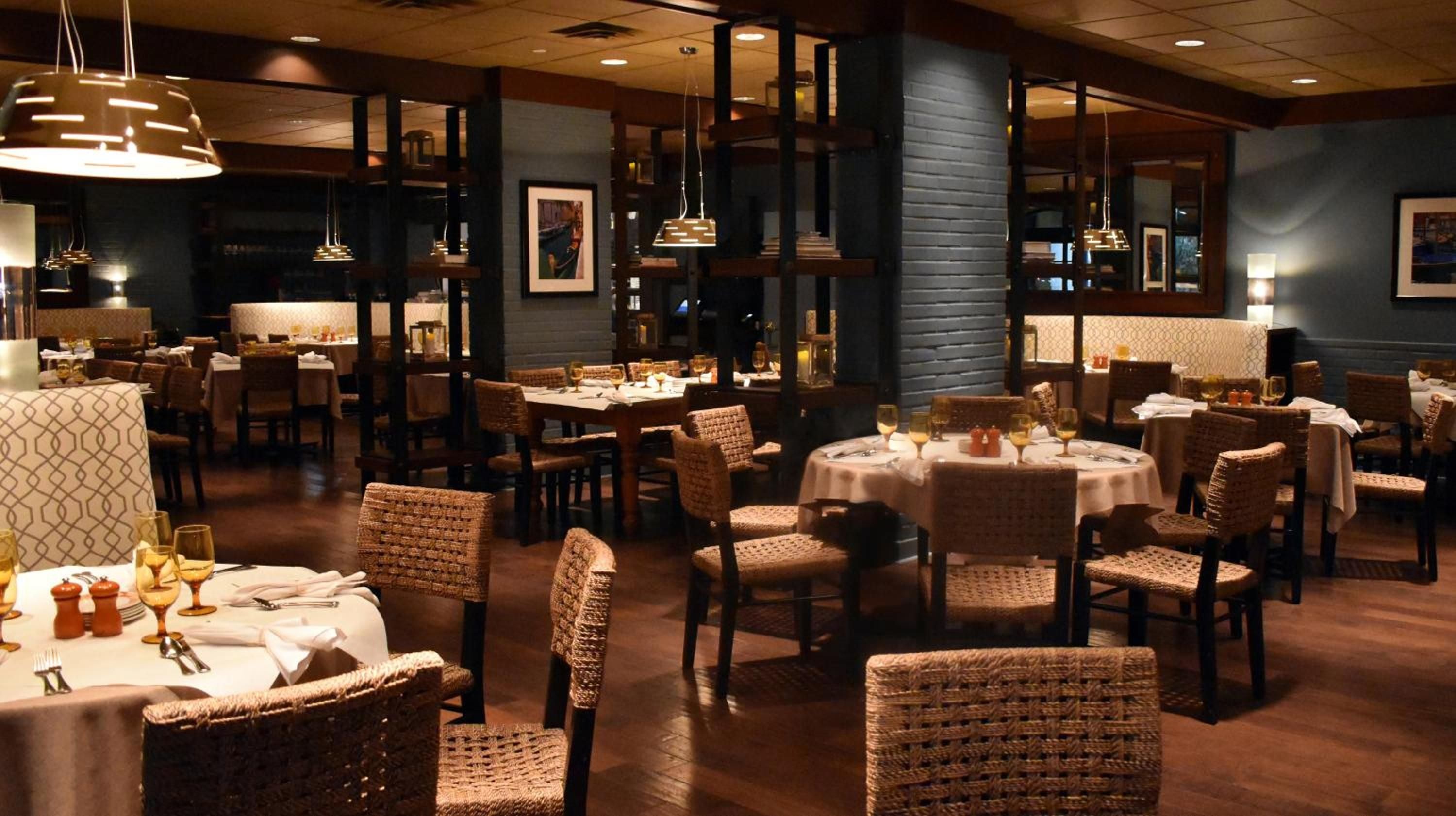 Wicker chairs and warm pendant lighting create an intimate dining atmosphere where crisp white tablecloths contrast beautifully against rich navy walls and polished dark floors.