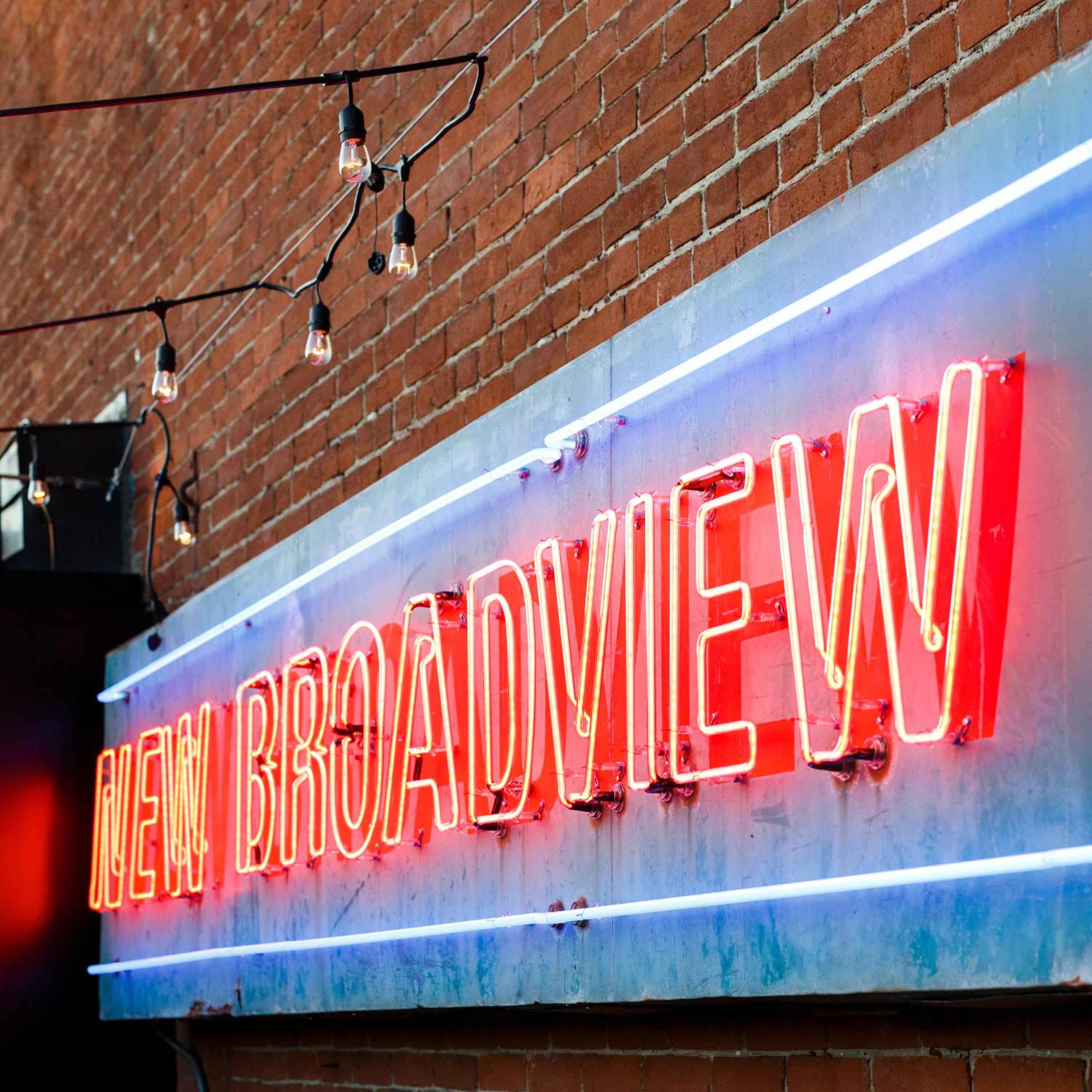 Glowing red neon letters spell out the hotel's name against weathered brick, while Edison bulbs cast a warm amber glow over this restored heritage facade.