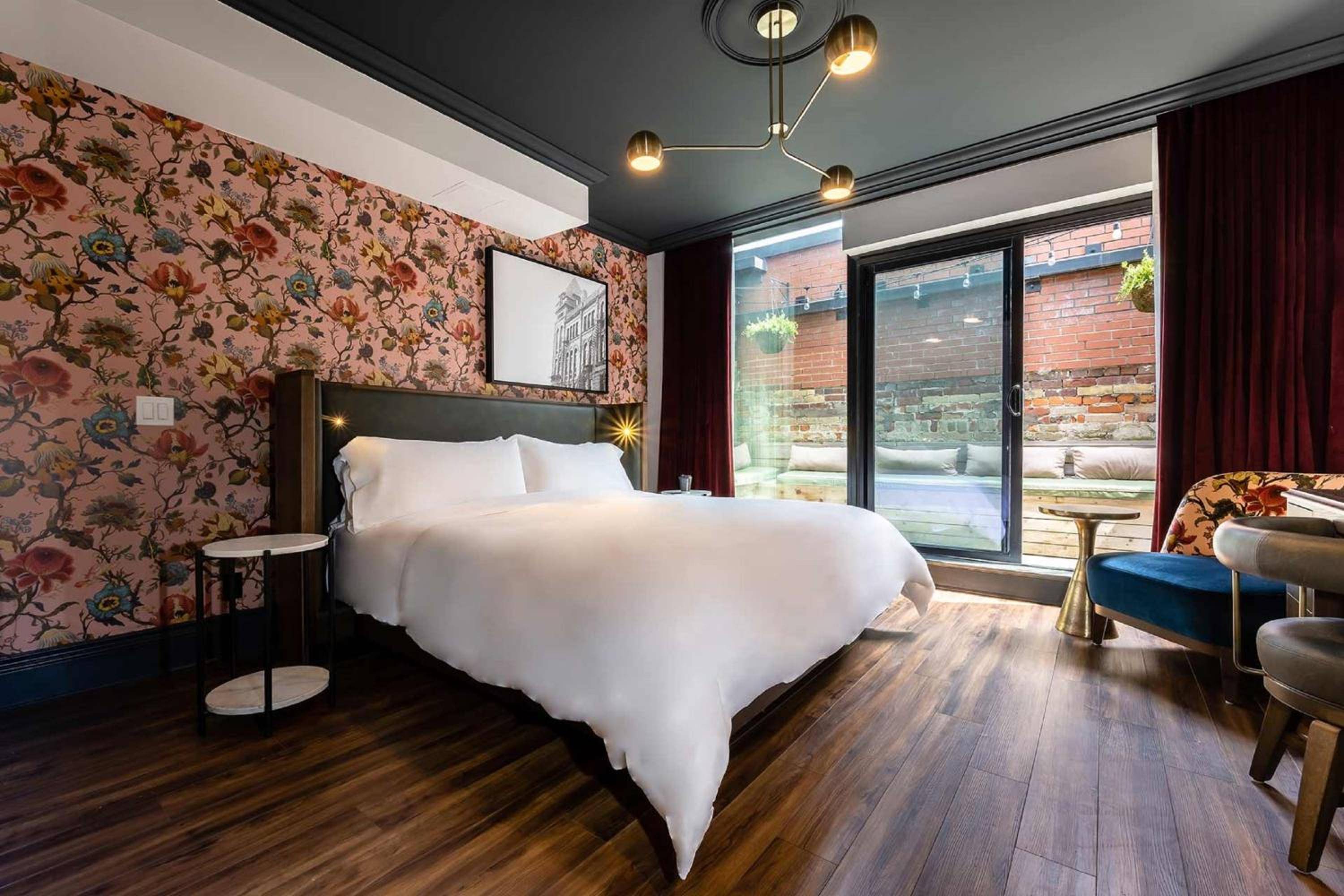 Bold floral wallpaper meets moody sophistication in this king suite, where brass fixtures cast warm light across rich hardwood floors and exposed brick views.