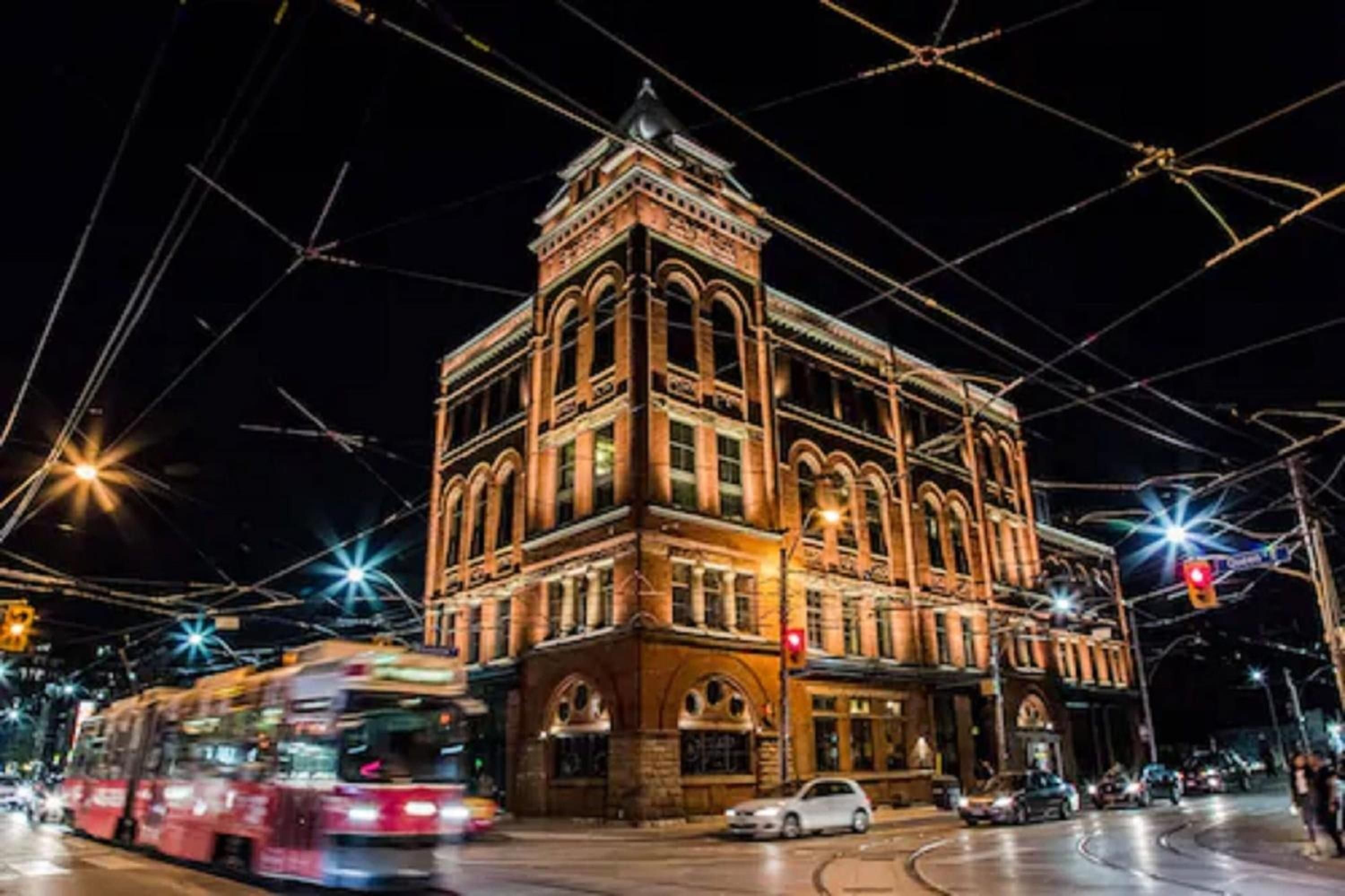 Victorian brick grandeur meets urban energy as streetcars glide past this magnificently restored corner landmark, its warm golden facade glowing against the night sky.