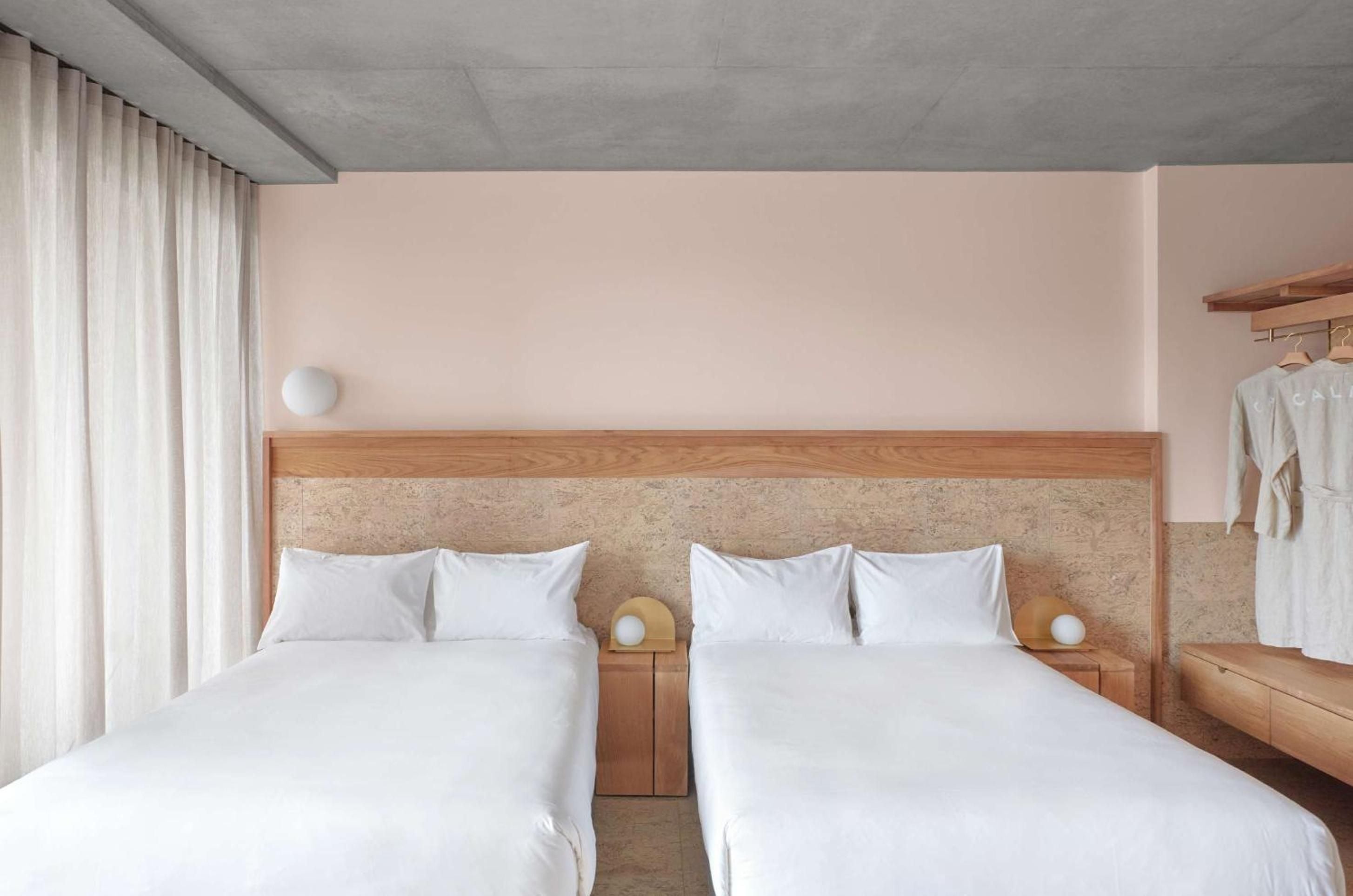 Twin beds nestle against cork-textured headboards in soft blush tones, where minimalist Japanese aesthetics meet warm Australian timber craftsmanship and gentle natural light.