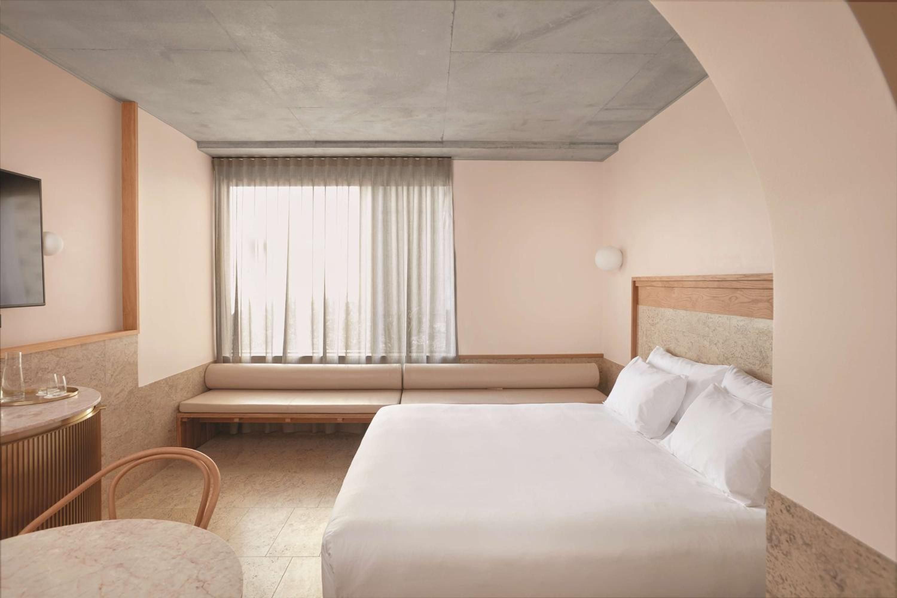 Warm terrazzo floors and blush-toned walls create an intimate cocoon, where concrete ceilings add industrial edge to the hotel's signature minimalist luxury aesthetic.