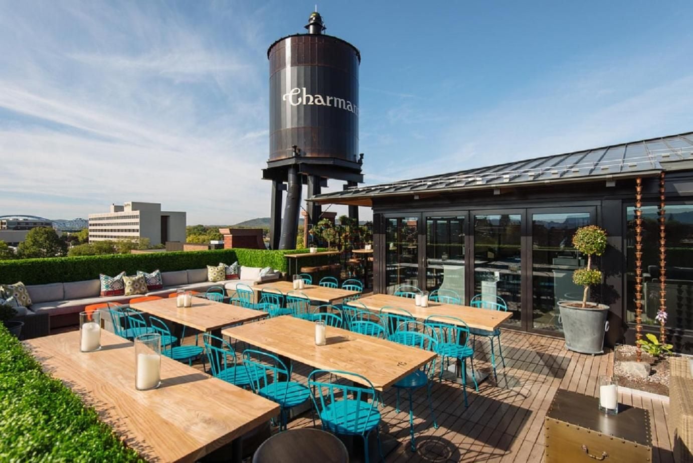 Turquoise chairs and weathered wood tables create an inviting rooftop dining scene, while the historic water tower stands sentinel over this elevated urban retreat.