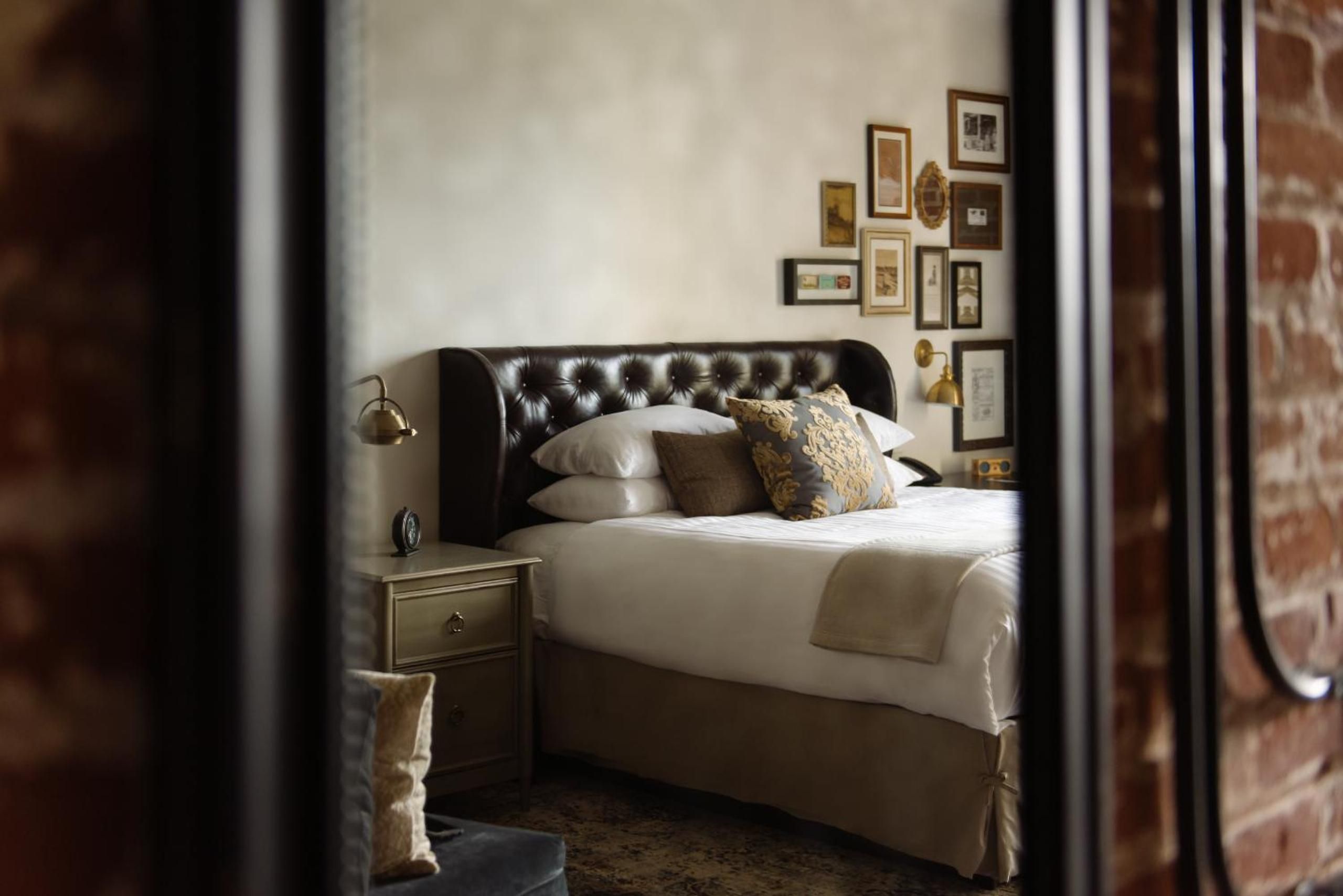 Tufted leather headboards and gallery walls create intimate sophistication in guest quarters, where brass sconces cast warm light across crisp linens and vintage-inspired furnishings.