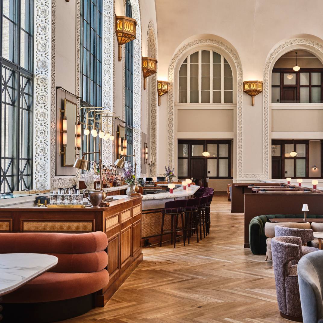 Soaring ceilings and intricate plasterwork frame the grand bar, where herringbone floors and jewel-toned seating create an atmosphere of refined elegance beneath ornate Moorish-inspired details.