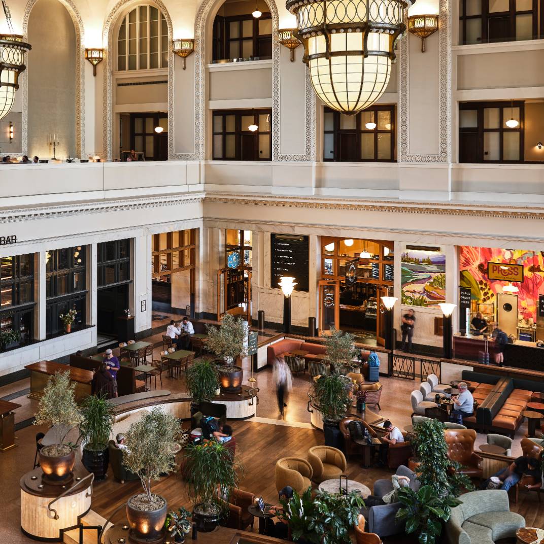 Soaring ceilings and ornate chandeliers frame the grand lobby's inviting seating areas, where travelers gather beneath intricate architectural details and warm ambient lighting.
