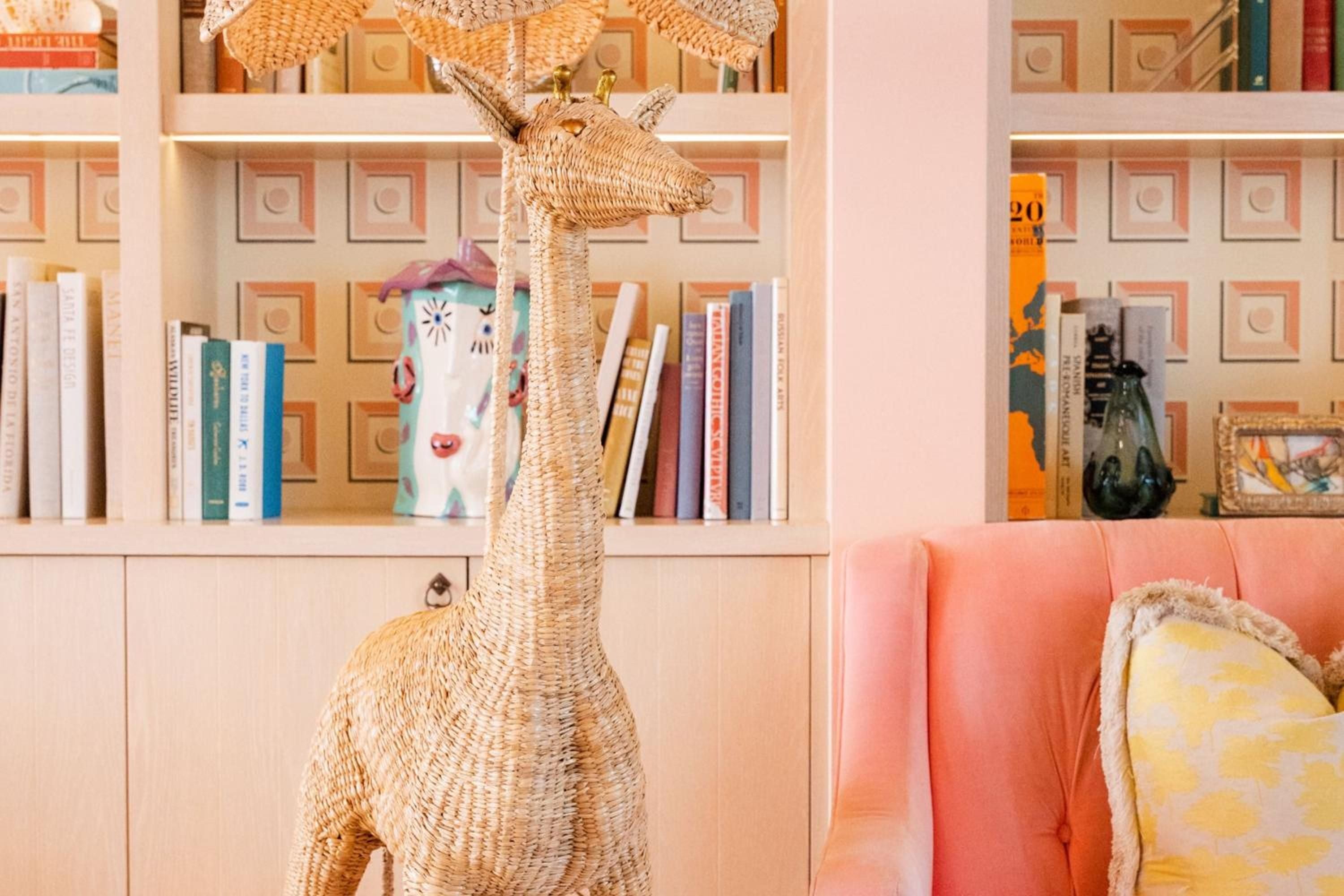 Woven rattan giraffe sculptures add whimsical charm to coral-hued reading nooks, where golden light bathes carefully curated bookshelves and plush velvet seating invites lingering.