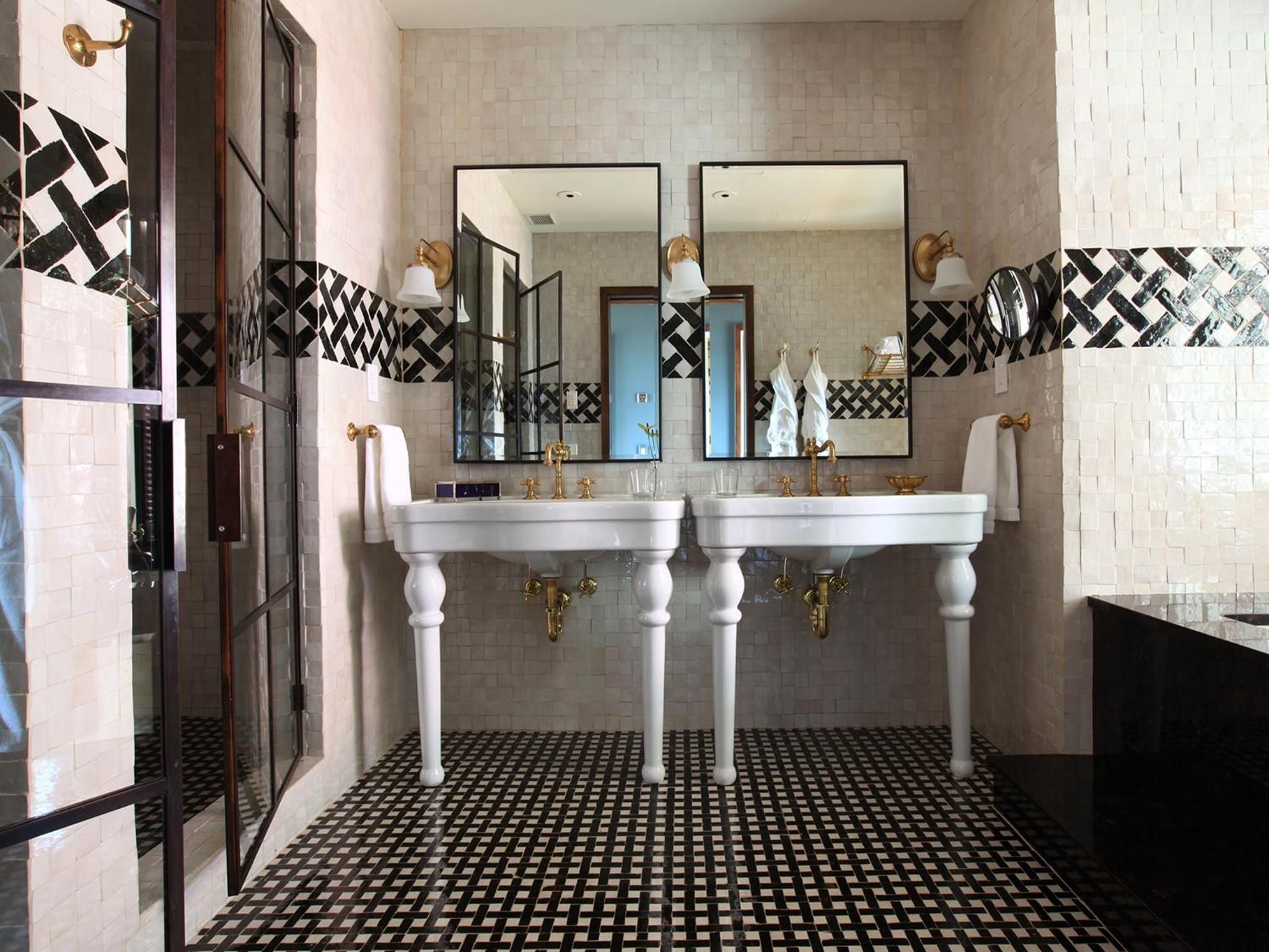 Geometric black-and-white tiles create striking patterns in this sophisticated dual-vanity bathroom, where brass fixtures and pedestal sinks evoke timeless European elegance.
