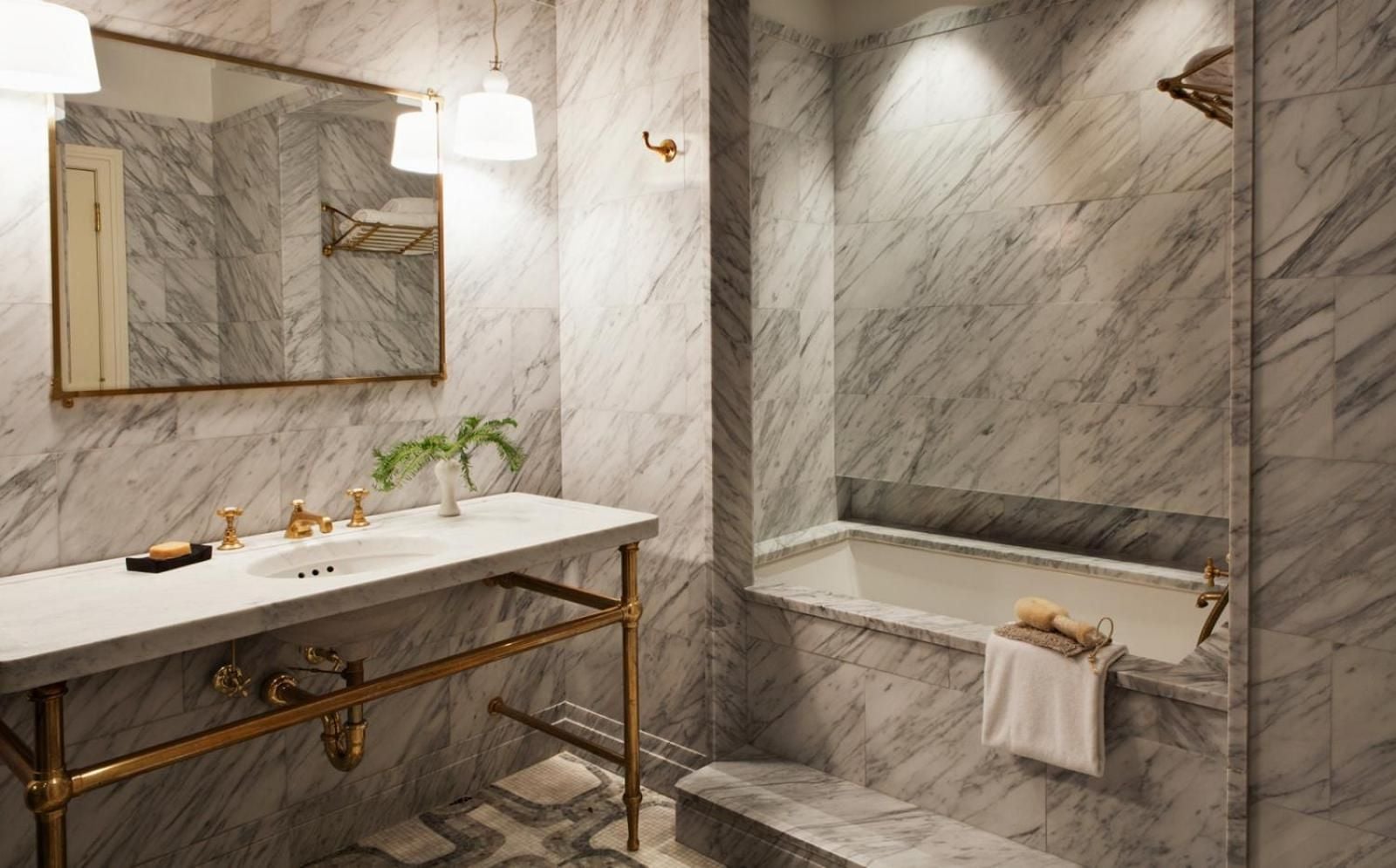 Carrara marble envelops this sumptuous bathroom in cool elegance, where brass fixtures catch the light and a deep soaking tub promises pure indulgence.