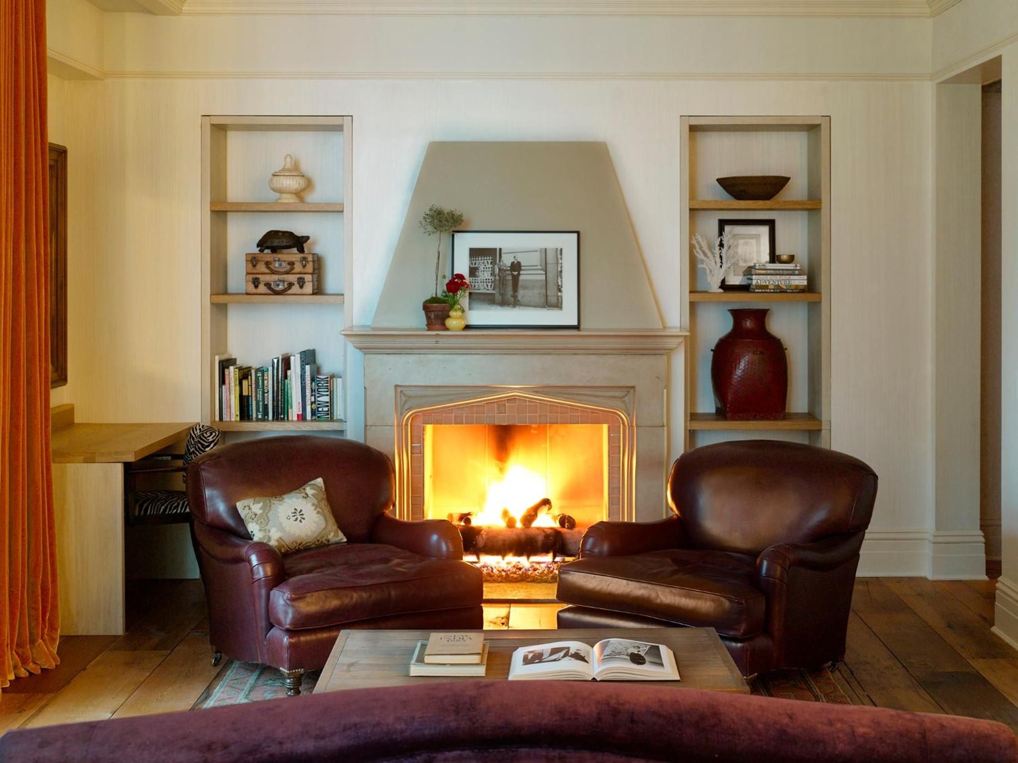 Rich leather armchairs flank a crackling fireplace, while built-in shelves display carefully curated ceramics and well-worn books in this intimate reading nook.