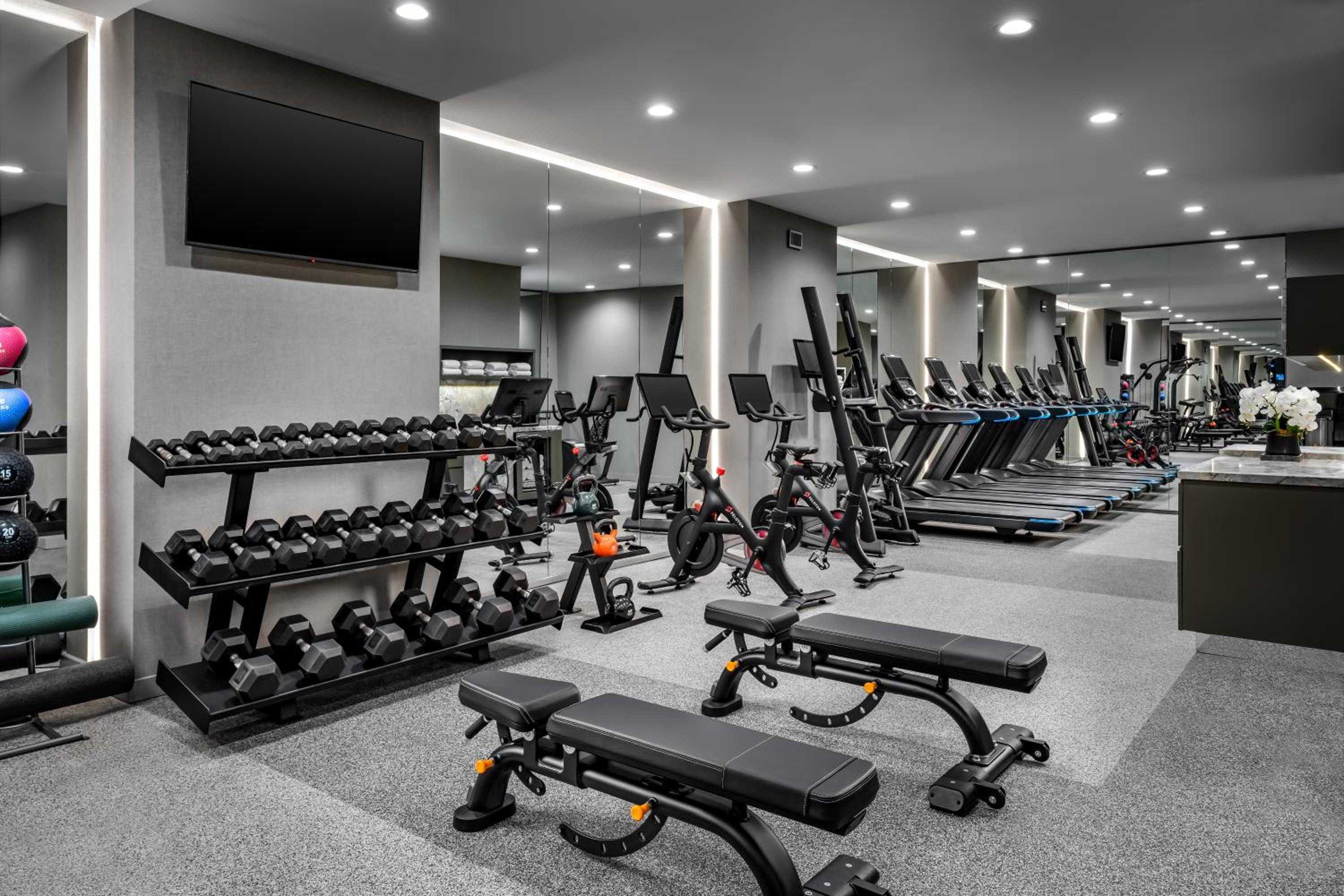Floor-to-ceiling mirrors amplify the spacious fitness center where polished dumbbells and sleek cardio equipment create an energizing sanctuary beneath crisp LED lighting.