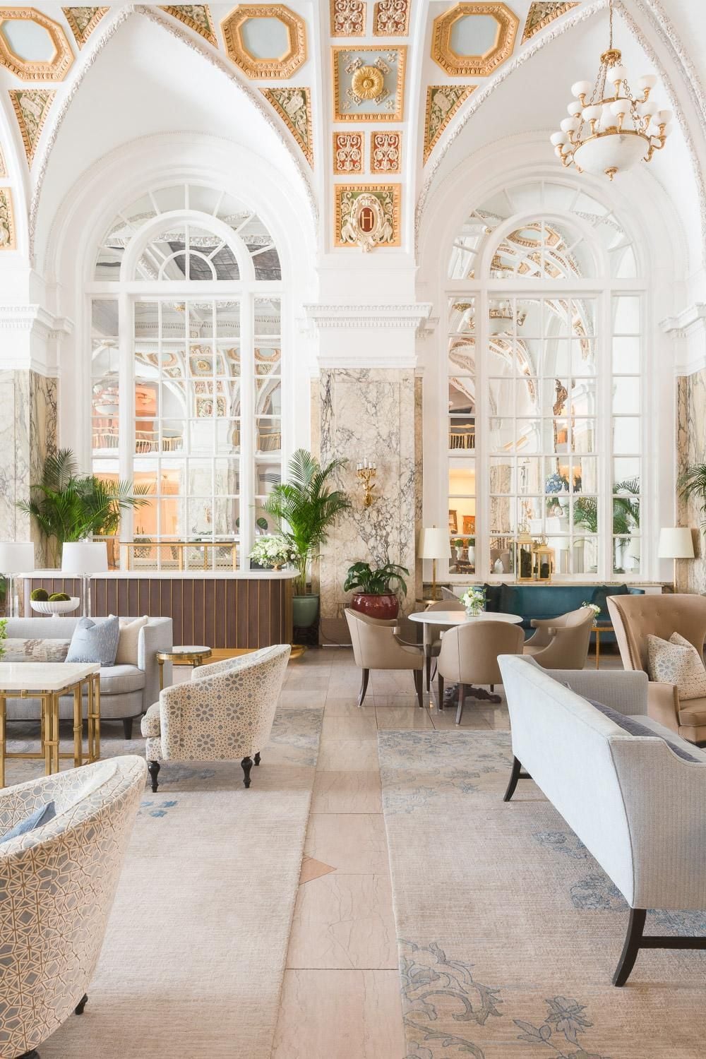 Soaring coffered ceilings adorned with gold leaf frame elegant seating vignettes, where marble columns and arched windows create an atmosphere of timeless grandeur.