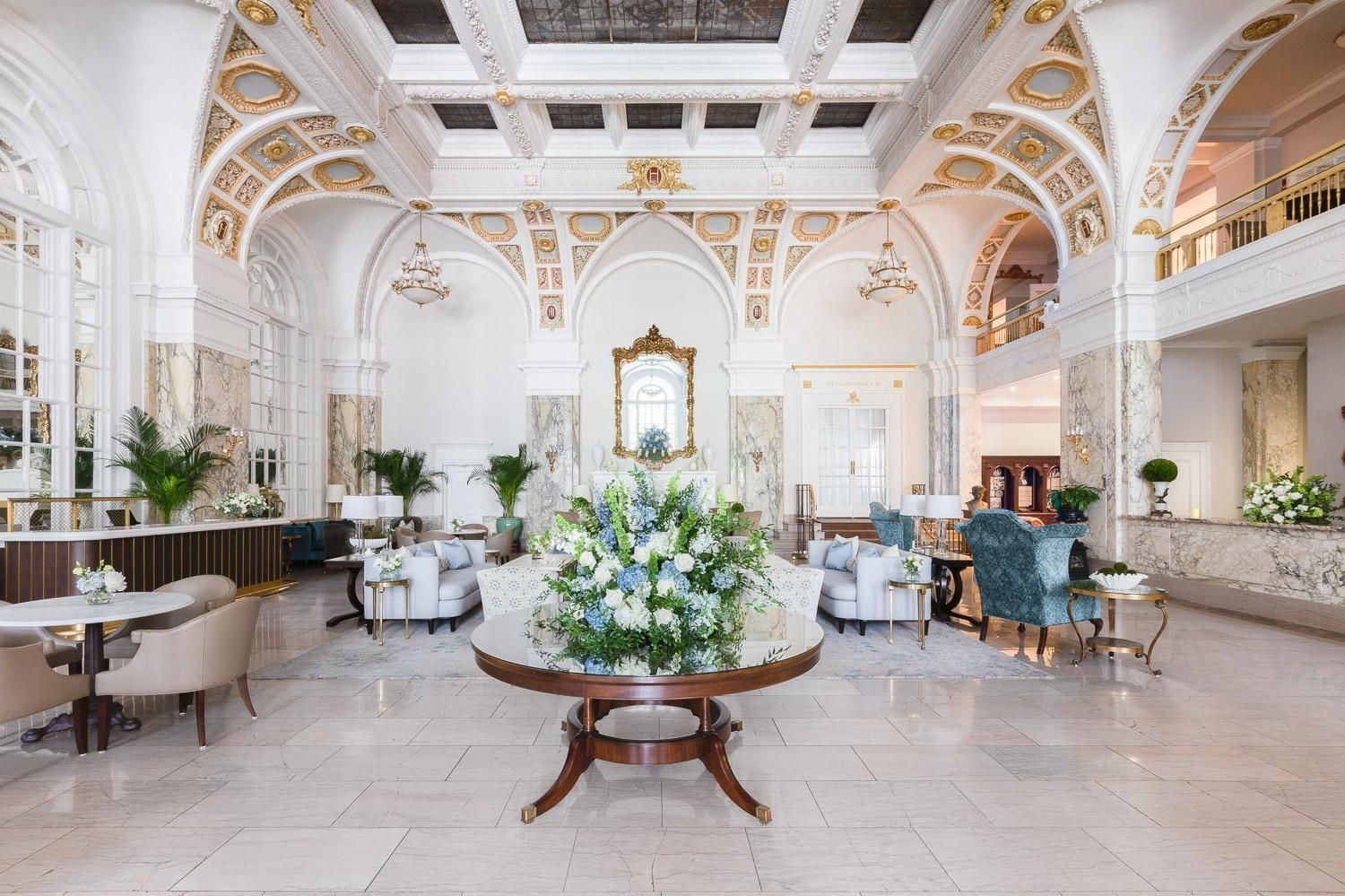 Gilded arches and marble columns frame The Hermitage's palatial lobby, where crystal chandeliers cast warm light over plush seating and cascading floral arrangements.