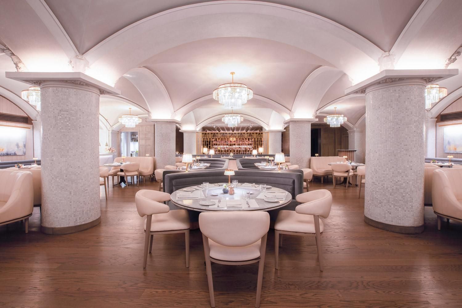 Barrel-vaulted ceilings and crystal chandeliers create cathedral-like grandeur in the dining room, where blush velvet chairs gather around intimate tables on rich hardwood floors.