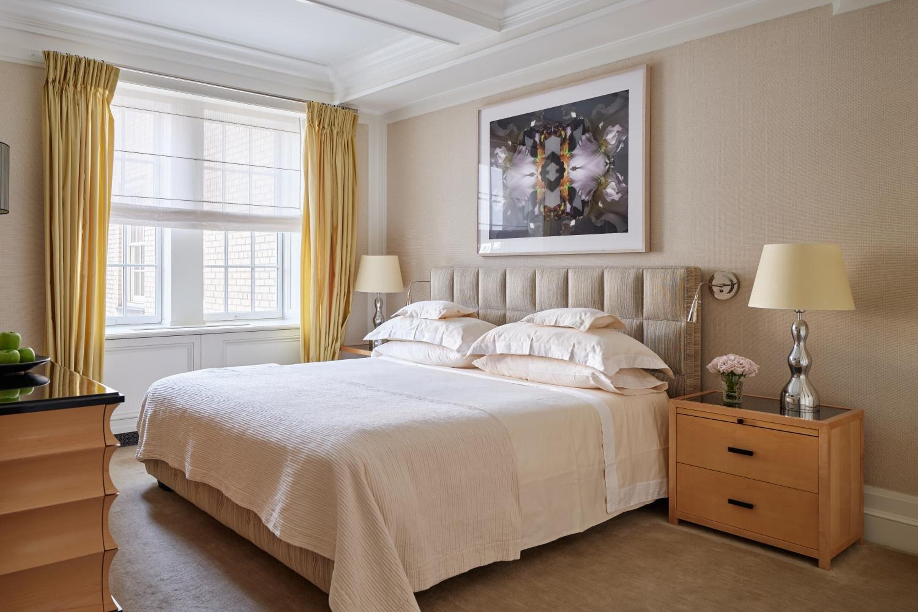 Cream linens and golden curtains create a cocoon of warmth in this sophisticated guest room, where coffered ceilings and textured walls whisper quiet luxury.