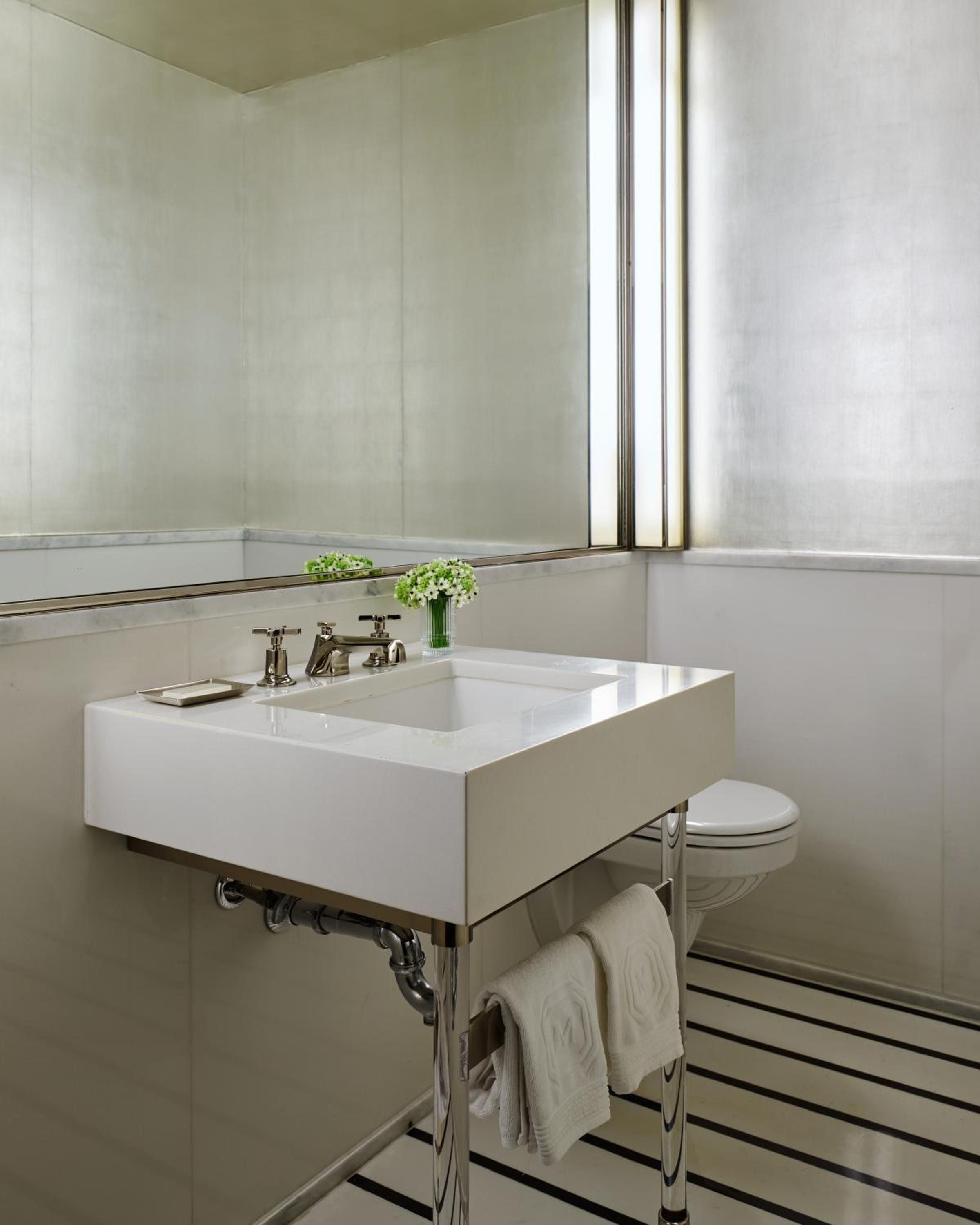 Minimalist luxury defines this powder room where polished marble meets sleek chrome fixtures, while soft natural light filters through frosted glass creating an intimate sanctuary.