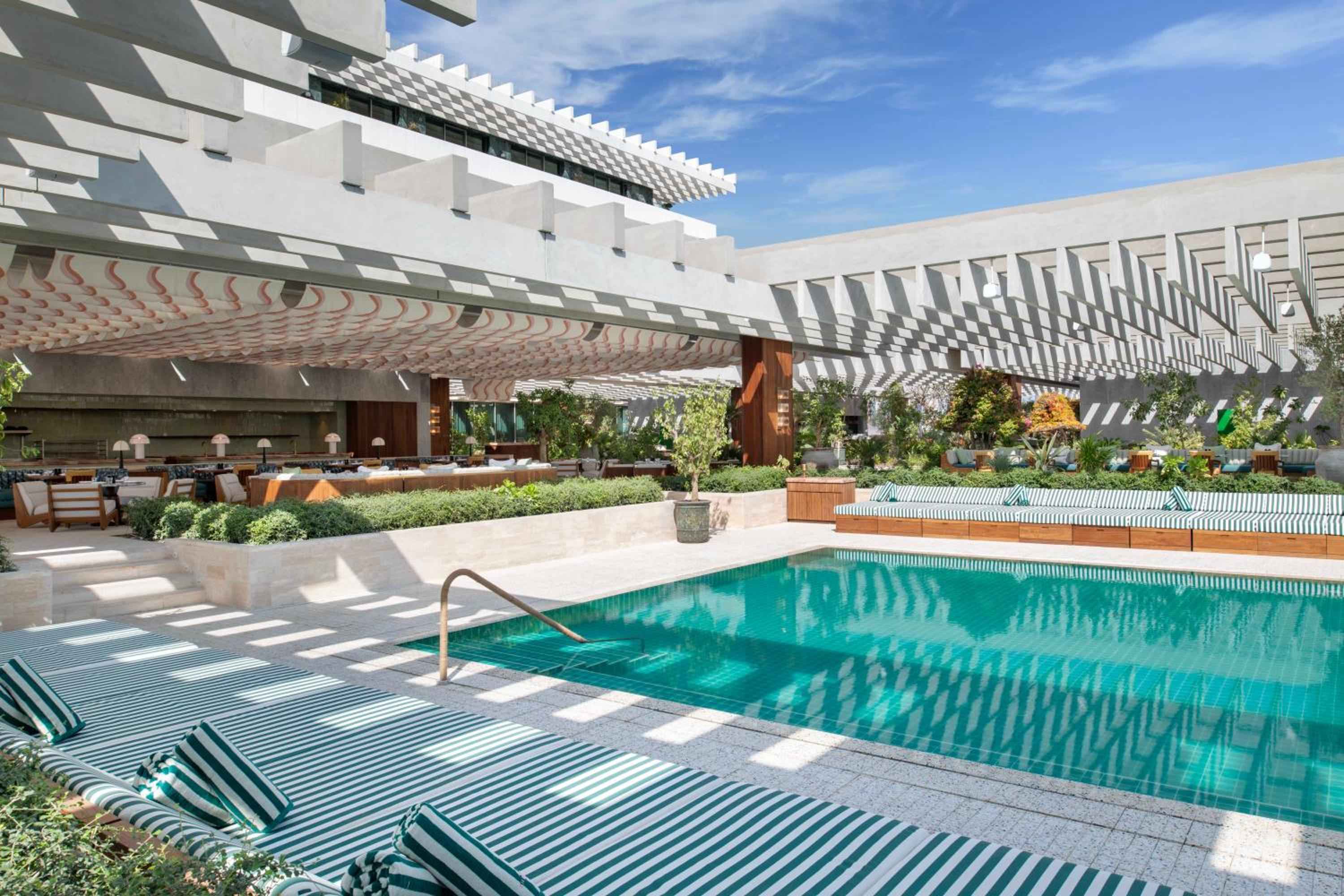 Geometric shadows dance across turquoise waters beneath soaring white pergolas, where striped loungers invite languid afternoons in this sophisticated indoor-outdoor oasis.