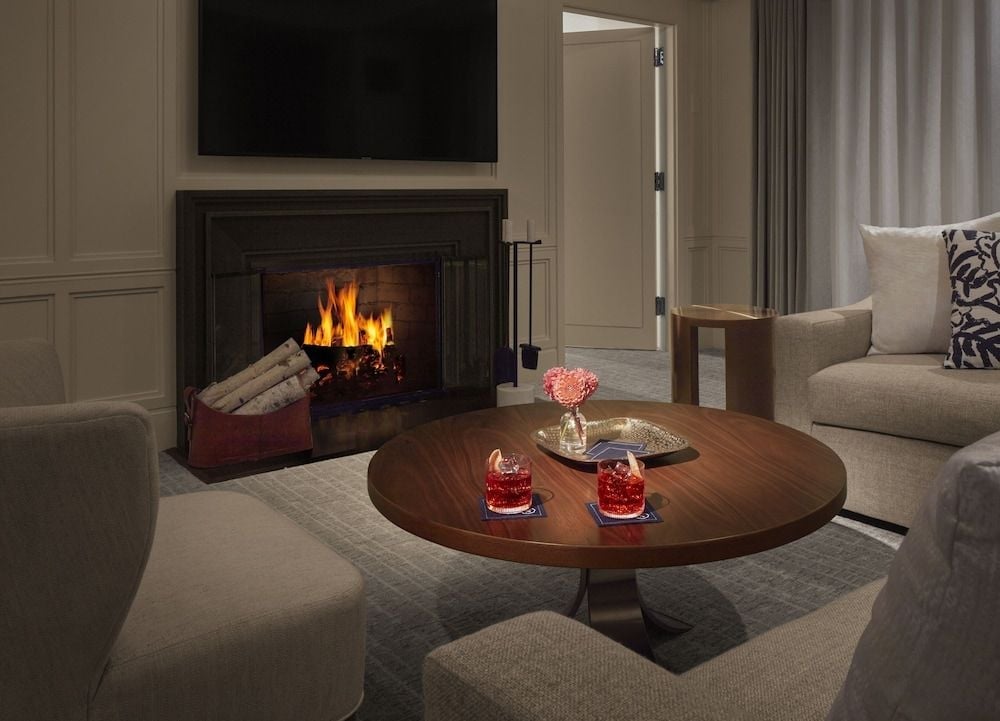 Flames dance behind wrought iron as amber light bathes plush seating and polished walnut, where red crystal catches firelight in this refined living space.