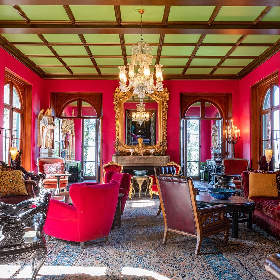 Crimson walls glow beneath an ornate coffered ceiling, where crystal chandeliers illuminate plush velvet chairs and gilded mirrors in this opulent drawing room.