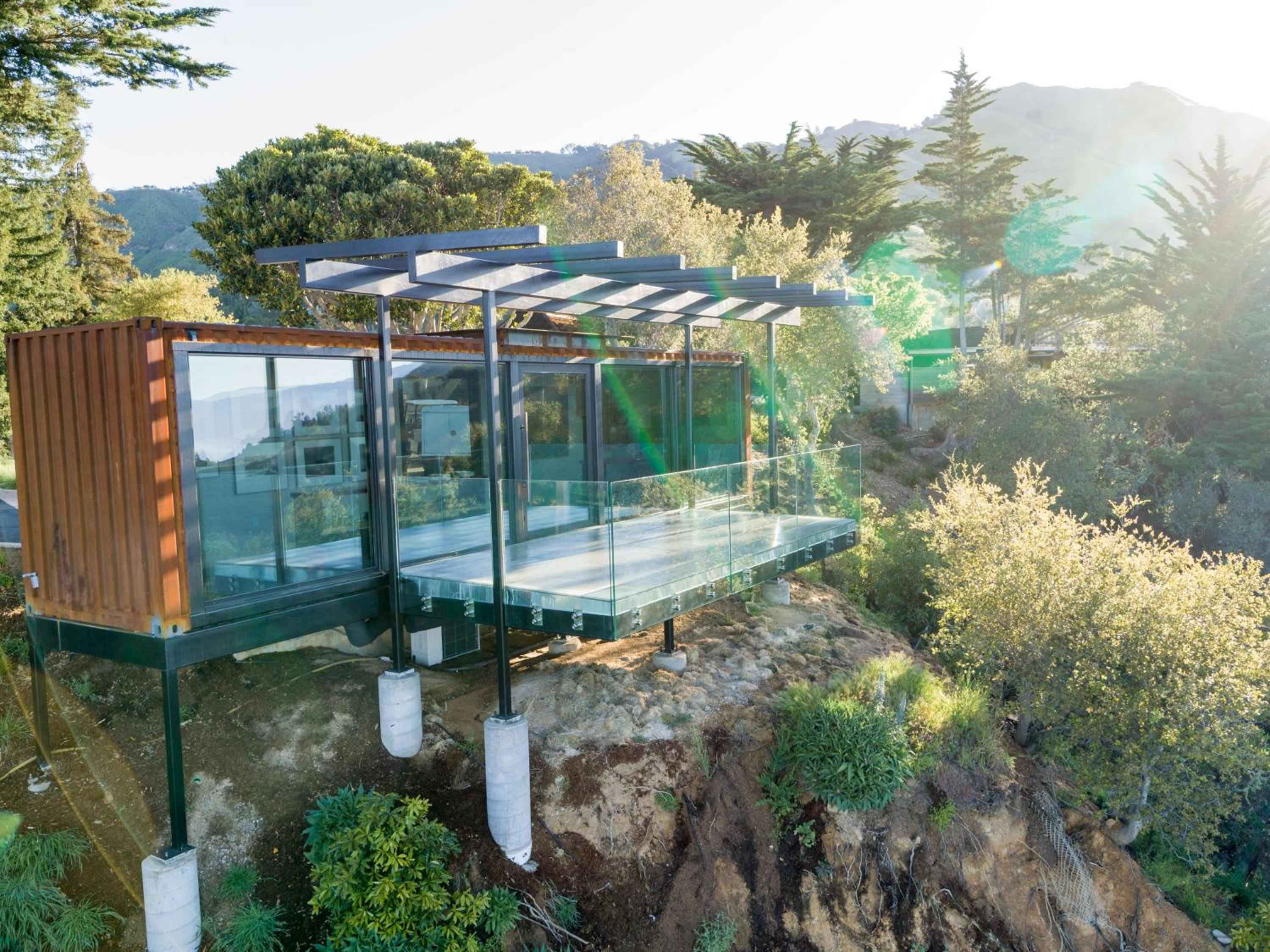 Glass-walled tree house suites perch on stilts among towering redwoods, their floor-to-ceiling windows framing Big Sur's misty canyon views in perfect morning light.