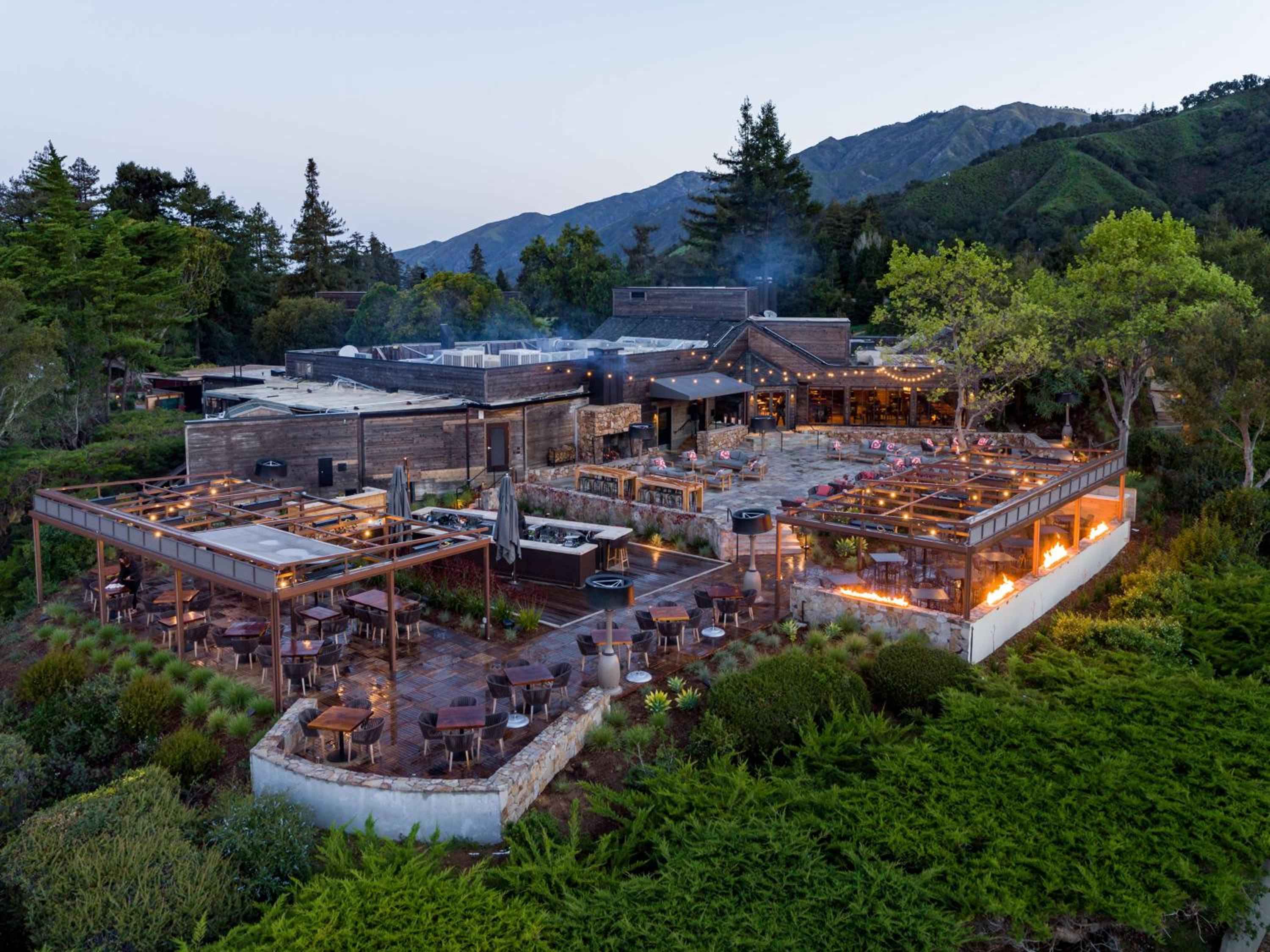 String lights illuminate the multi-level terrace restaurant as twilight settles over the Santa Lucia Mountains, creating an enchanting hillside dining sanctuary.