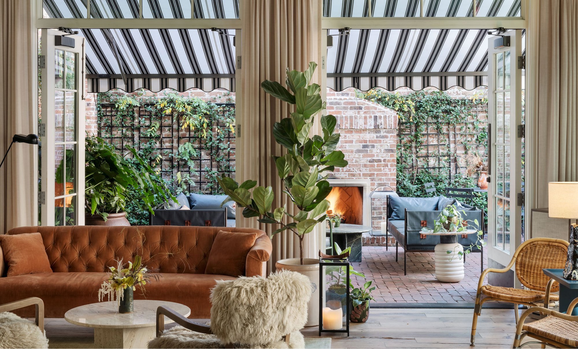 Sunlight filters through the conservatory-style ceiling onto butter-soft leather seating, while fiddle leaf figs frame views of the intimate brick courtyard with its glowing fireplace.