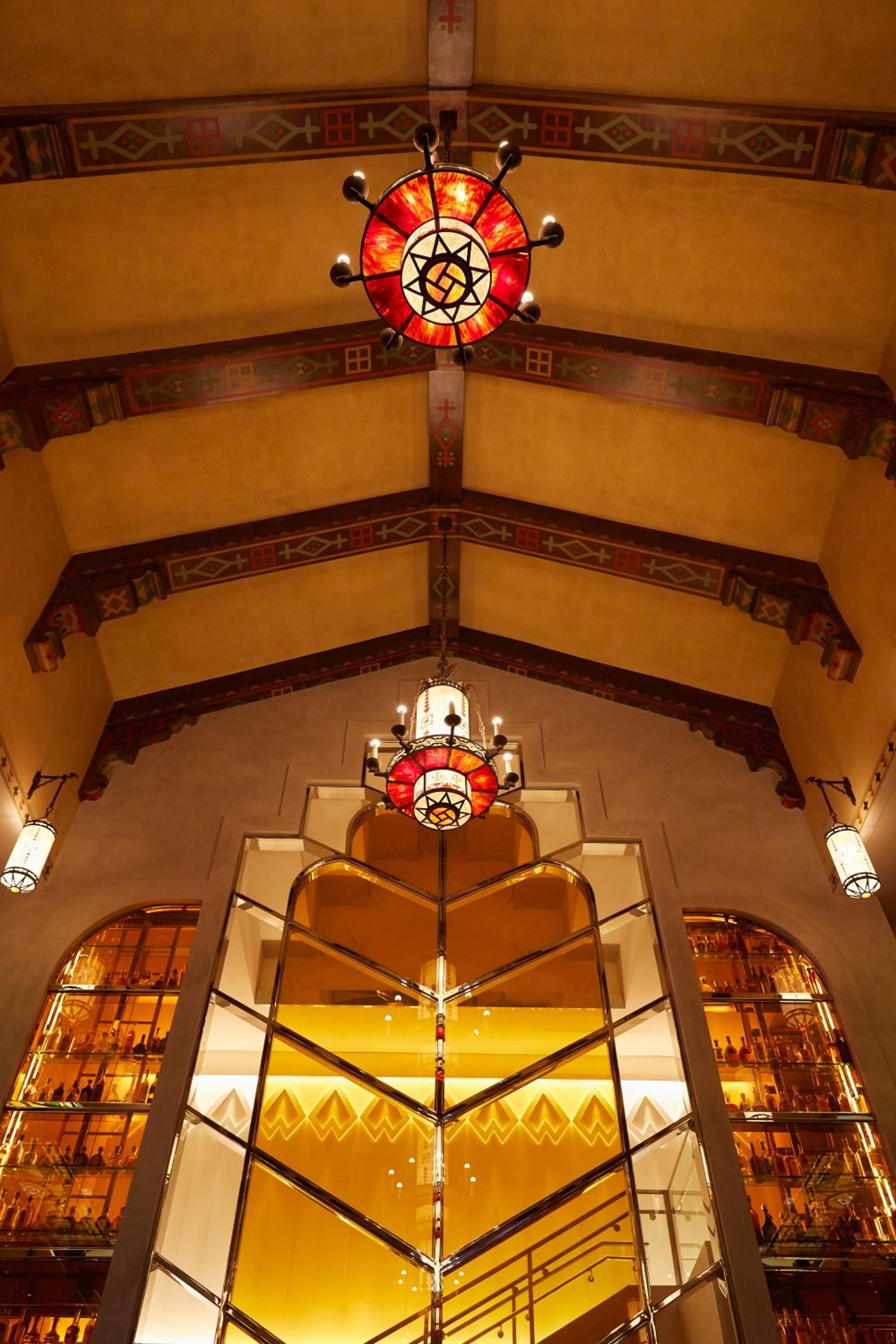 Soaring exposed beams frame ornate chandeliers and geometric patterns in this grand southwestern-inspired lobby, where warm amber light dances across hand-painted ceiling details.