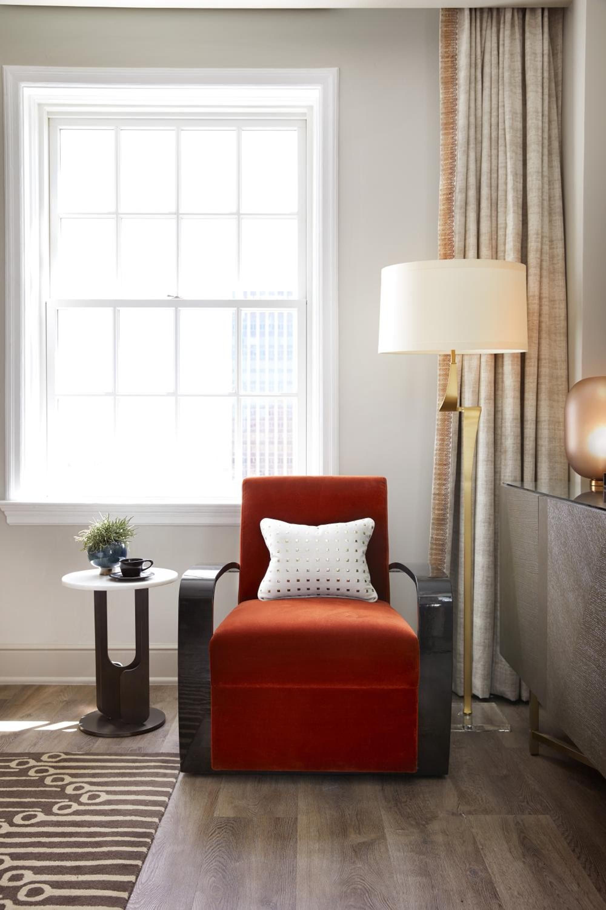 Burnt orange velvet meets brass accents in this thoughtfully curated corner, where natural light spills across polished hardwood and geometric patterns create visual warmth.