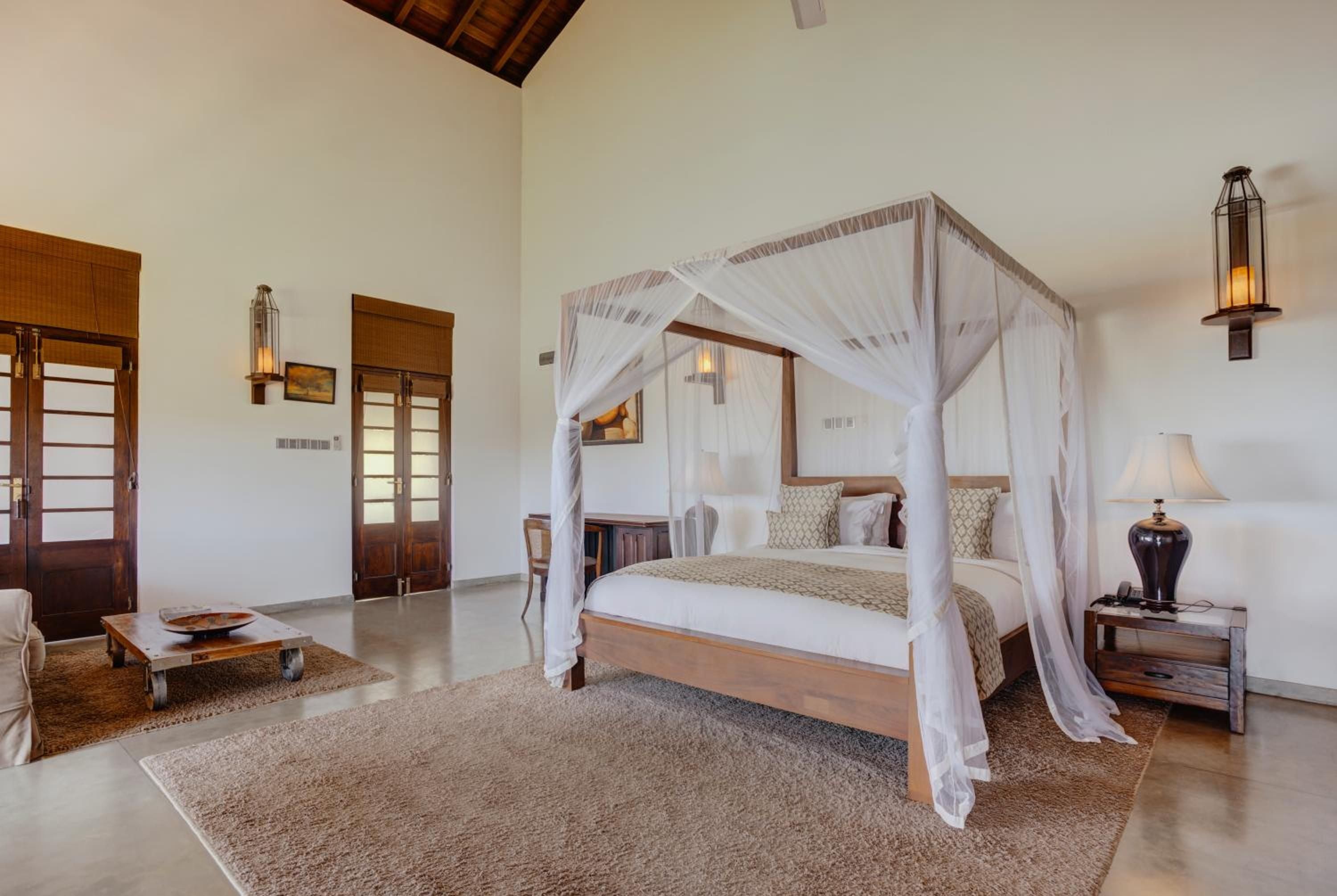 Flowing white mosquito nets frame a teak four-poster bed, while warm lantern light dances across polished concrete floors in this airy colonial-inspired suite.