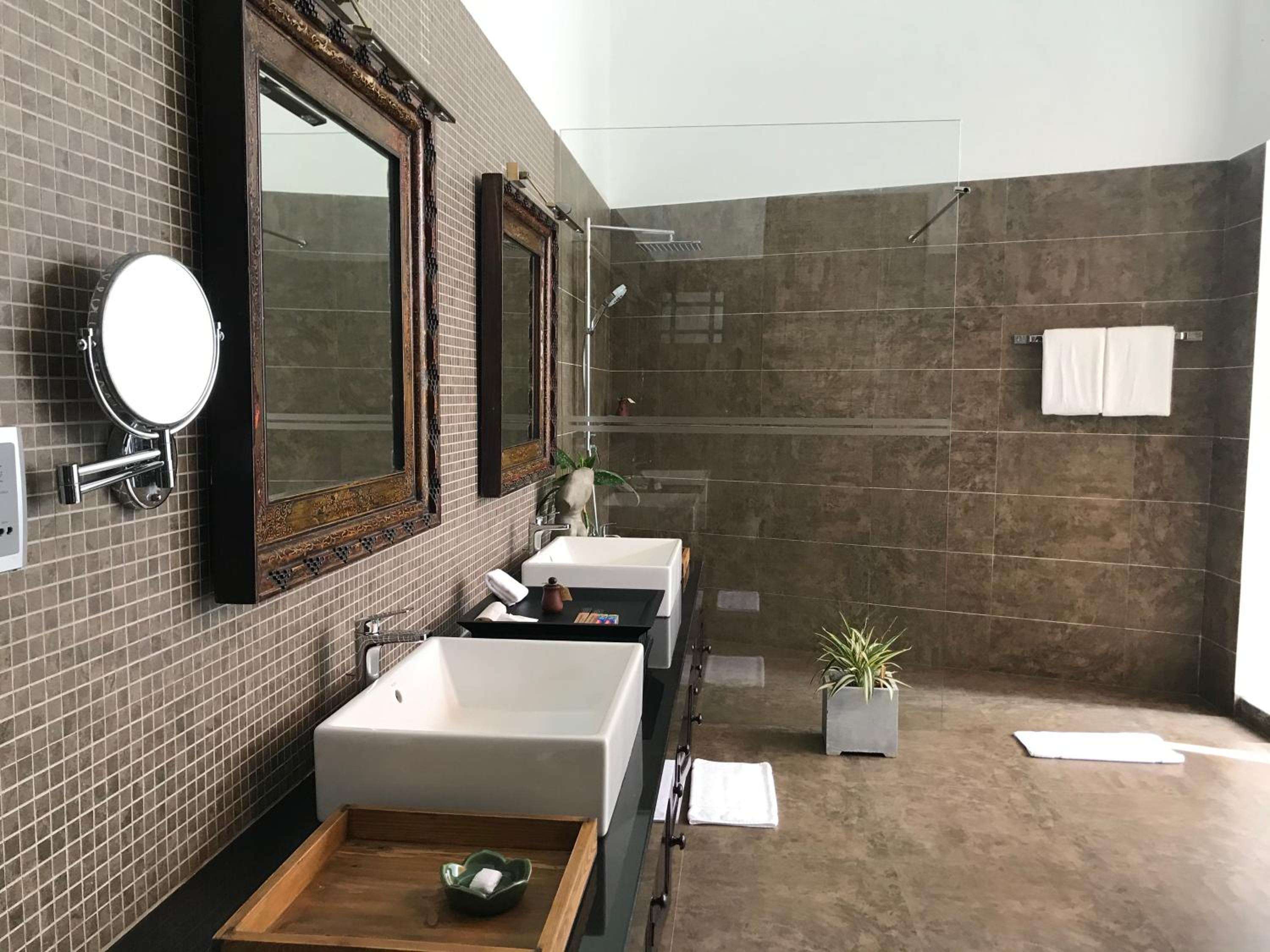 Modern vessel sinks float above dark timber vanities while mosaic tiles catch morning light streaming into this spa-inspired sanctuary with glass-enclosed rain shower.