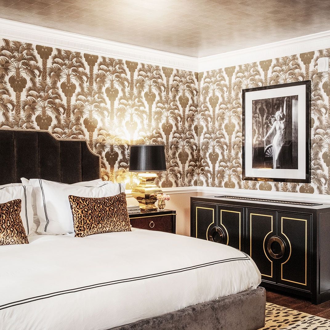 Gold palm frond wallpaper creates a glamorous backdrop for crisp white linens and leopard print accents, while warm lamplight casts an intimate Hollywood glow.