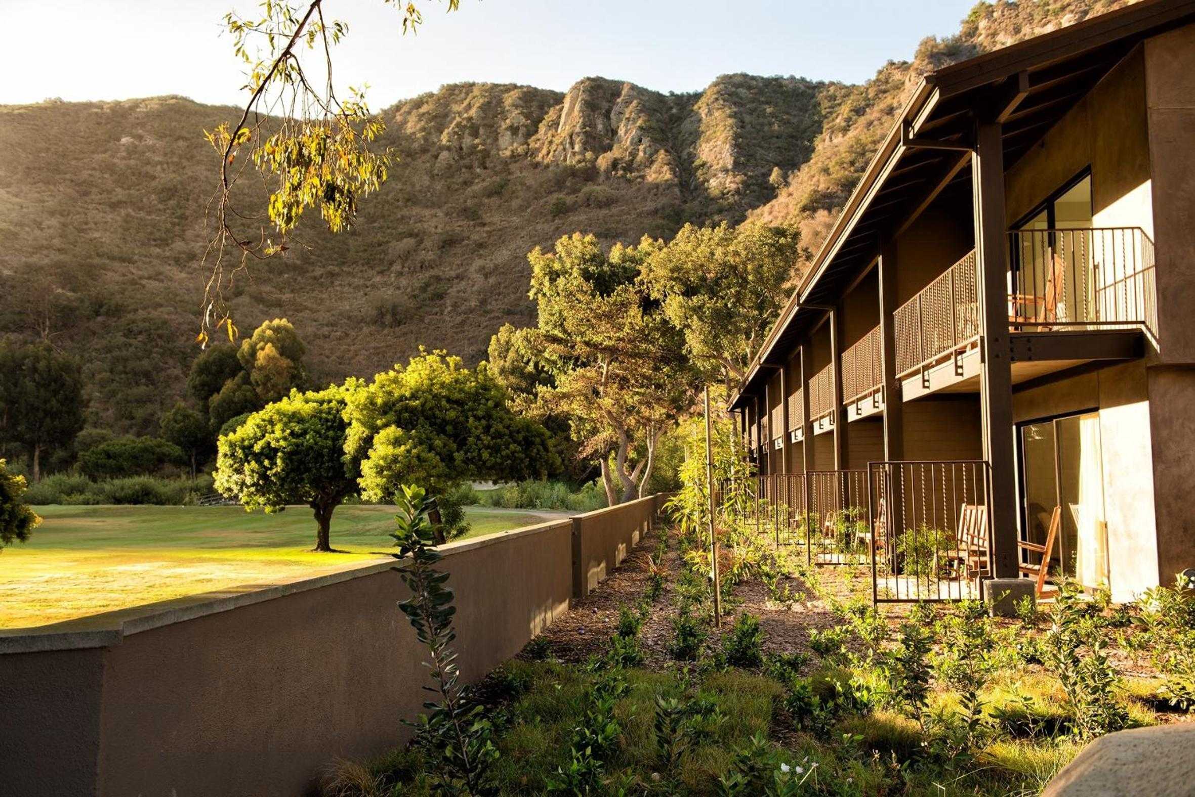 Golden hour illuminates terraced guest rooms where private balconies overlook manicured lawns and the rugged Santa Monica Mountains beyond.
