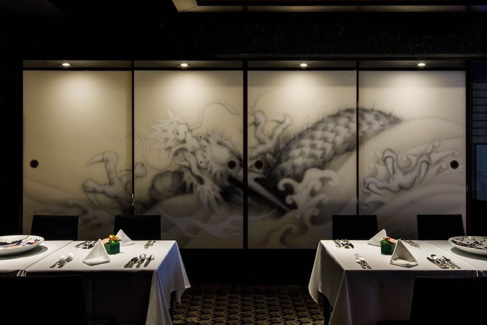 Dragon murals undulate across sliding screens in this intimate dining room, where traditional Japanese artistry meets contemporary elegance through dramatic lighting and pristine table settings.