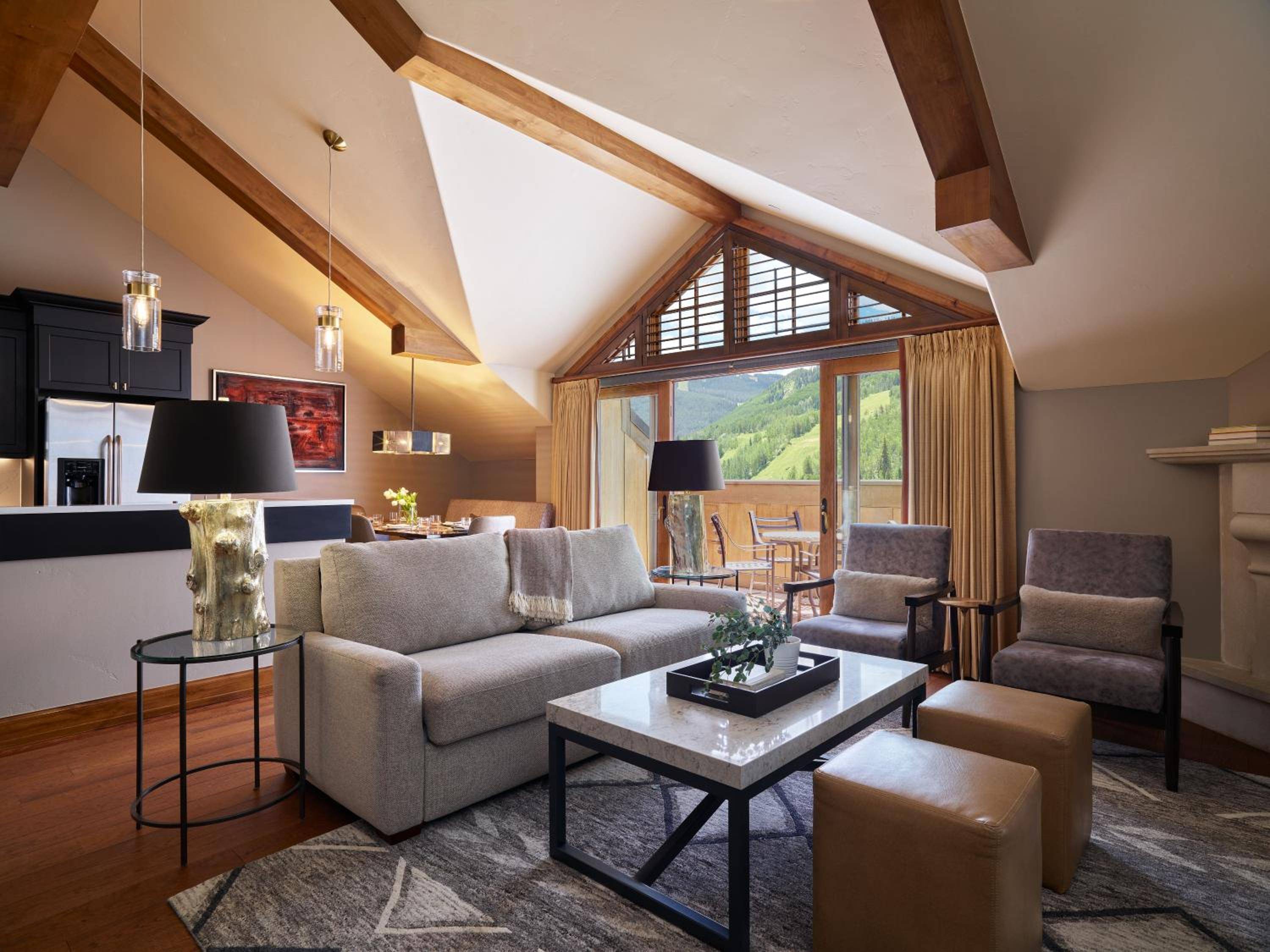 Exposed timber beams frame mountain vistas through floor-to-ceiling windows, while neutral furnishings and pendant lighting create an intimate alpine retreat high above Vail.