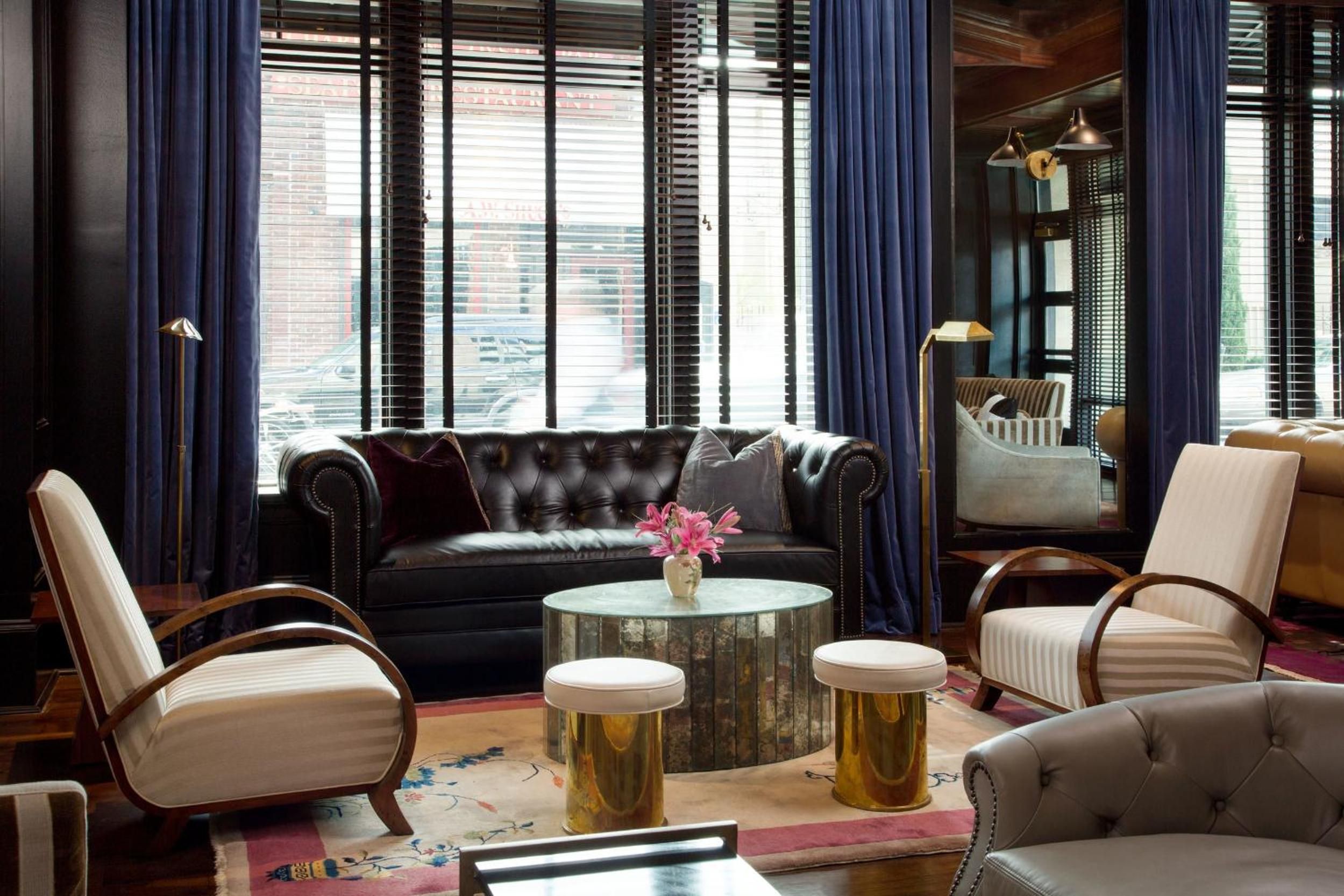 Rich navy curtains frame street views while golden stools gather around mirrored tables, creating an intimate salon where leather Chesterfields meet mid-century curves.