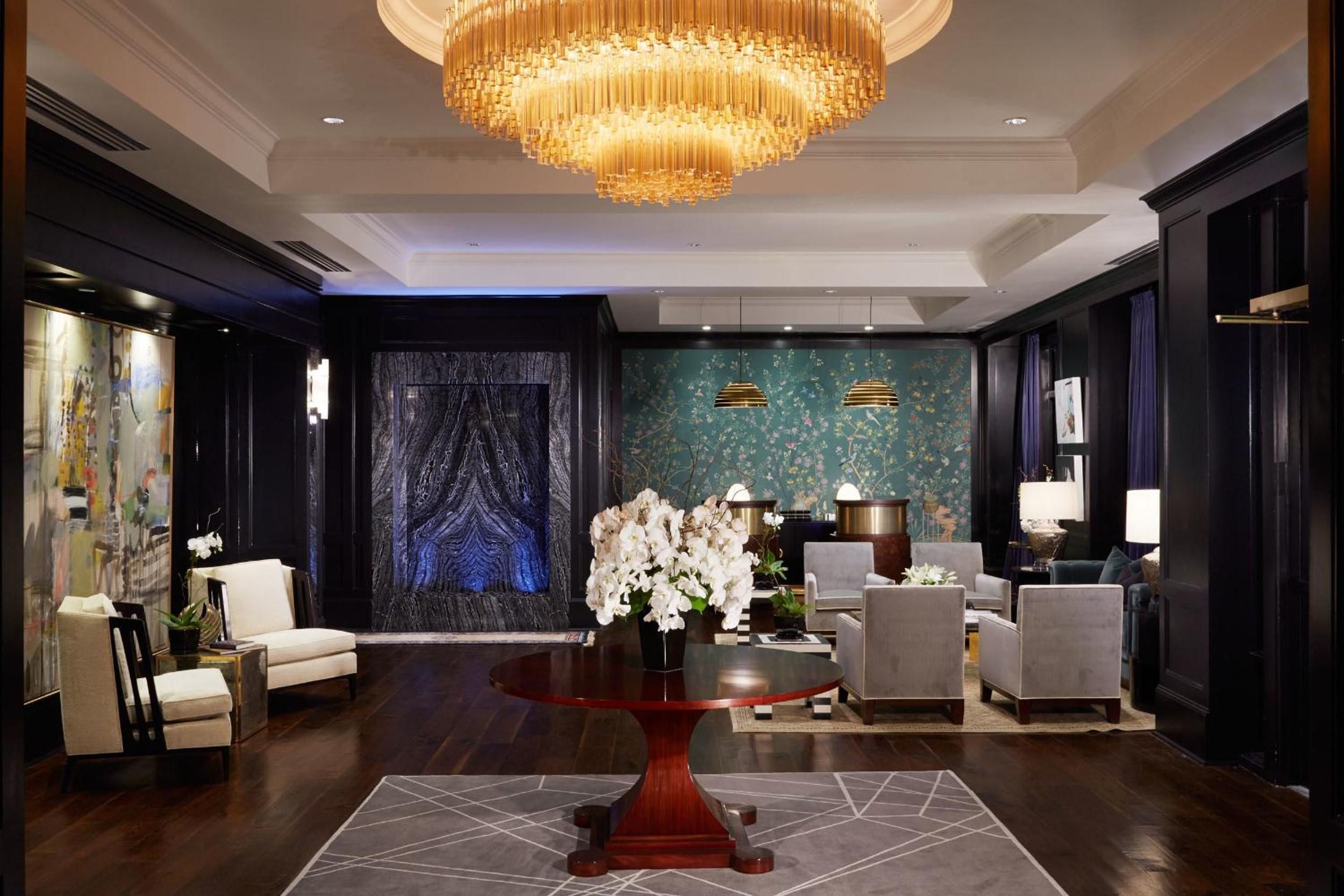 Crystal cascades from an amber chandelier while dark wood paneling frames jewel-toned chinoiserie wallpaper, creating an intimate gathering space that whispers old-world Charleston elegance.